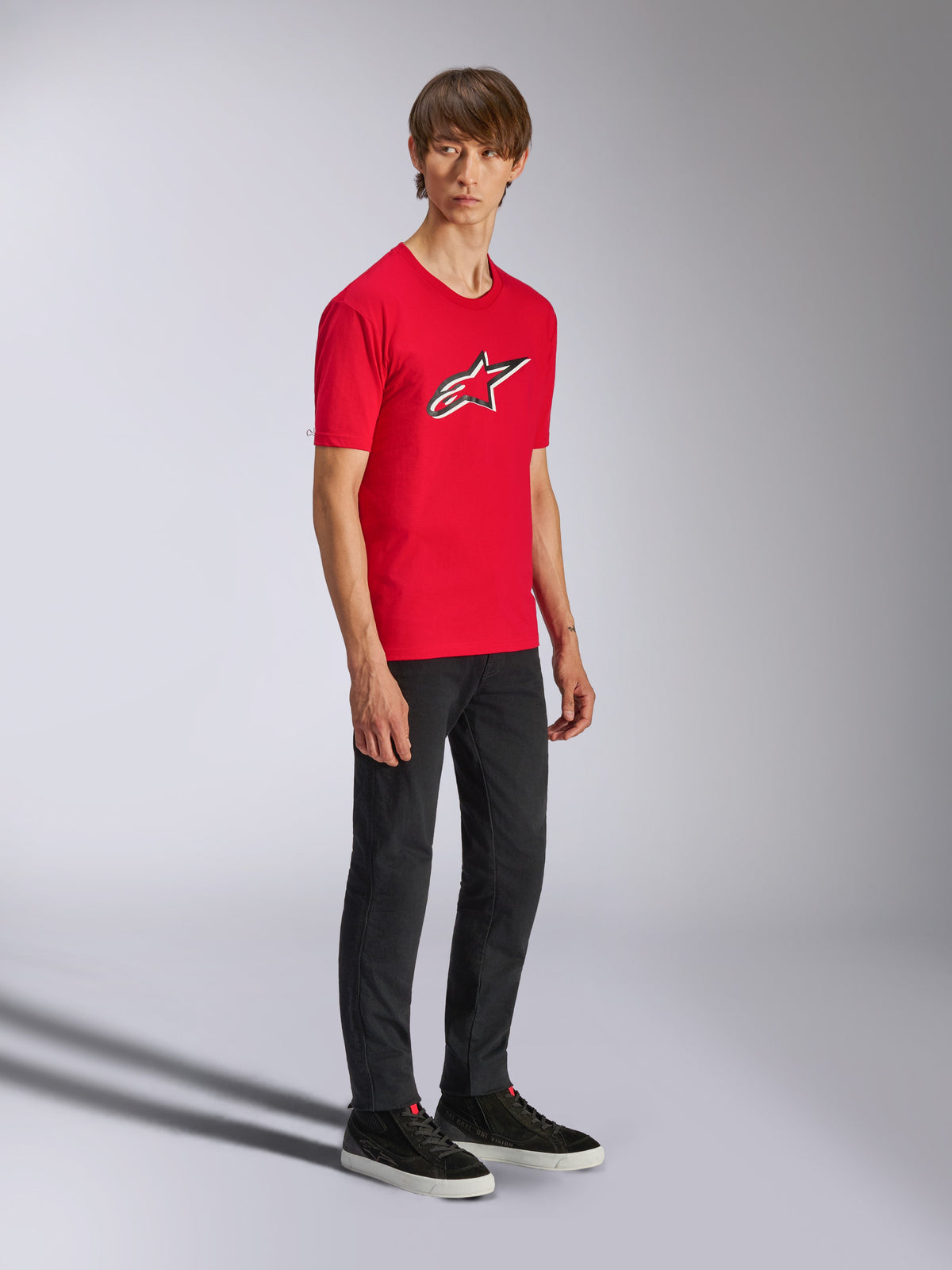 Alpinestars Ageless Shadow CSF Tee, Red Short Sleeve T-Shirt, featuring a large Ageless logo on the chest, worn by a model with black pants and sneakers, casual motorsport streetwear