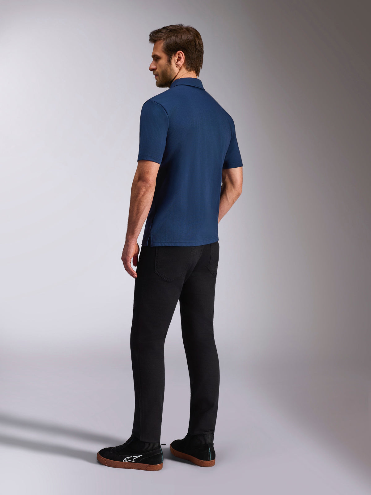 Alpinestars Impetus Sport Polo, Navy Blue Short Sleeve Polo Shirt, Back and side view on model, paired with black pants and black sneakers, casual motorsport lifestyle sportswear