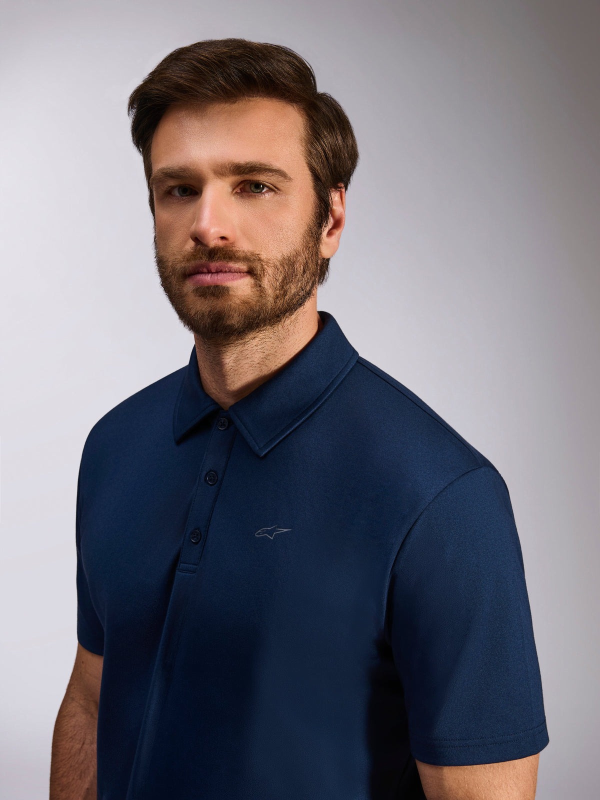 Model wearing Alpinestars Impetus Sport Polo, Navy Blue, mock mesh short sleeve polo shirt, featuring a three-button placket and subtle Astars logo on chest, casual motorsport lifestyle apparel