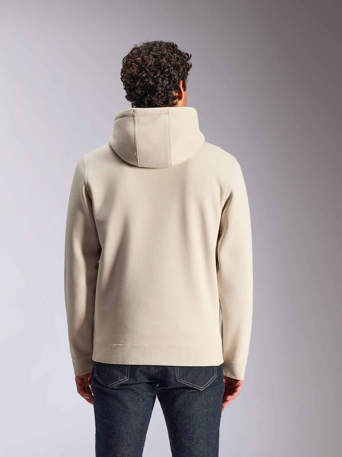 Alpinestars Pulse Hoodie, Sand color, back view of male model wearing the solid hooded pullover, paired with dark denim jeans, casual motorsport-inspired streetwear