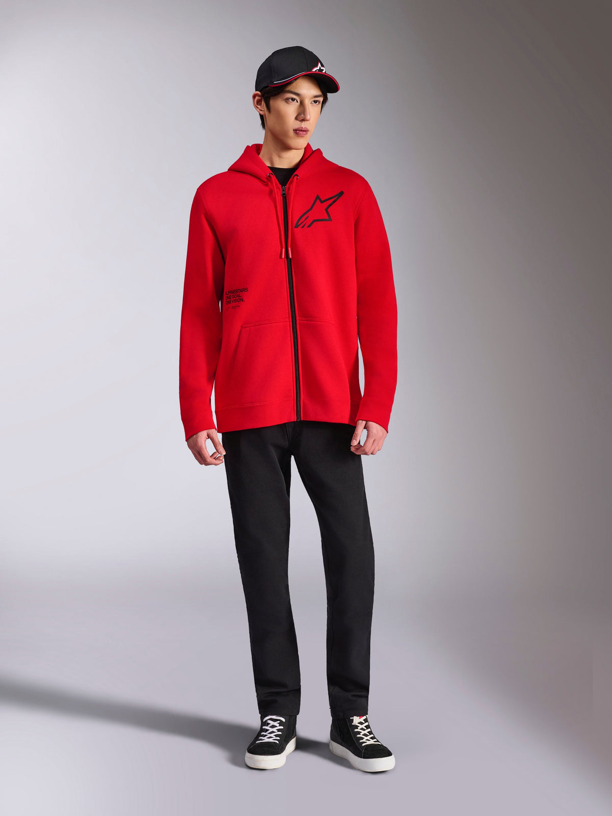 Alpinestars Transverse Hoodie, Red full-zip fleece hoodie, black Astars logo on chest and One Goal print on side, worn by male model with black pants and cap, casual motorsport-inspired streetwear