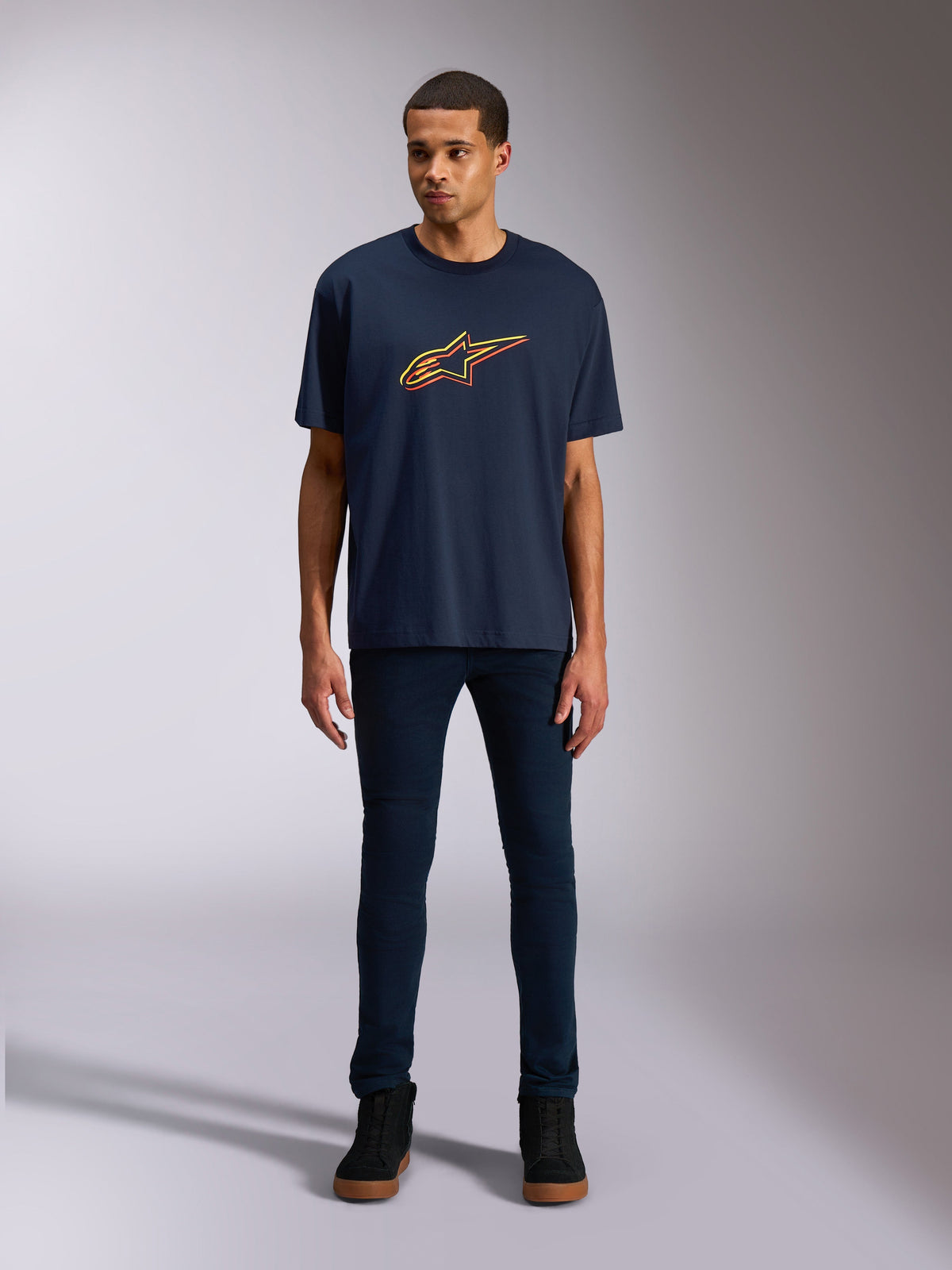 Alpinestars Alter Oversized CSF Tee, Short Sleeve T-Shirt, Navy Blue, featuring a front Alpinestars star logo with a yellow and orange color offset, worn by a model with dark denim and black sneakers, casual lifestyle sportswear.