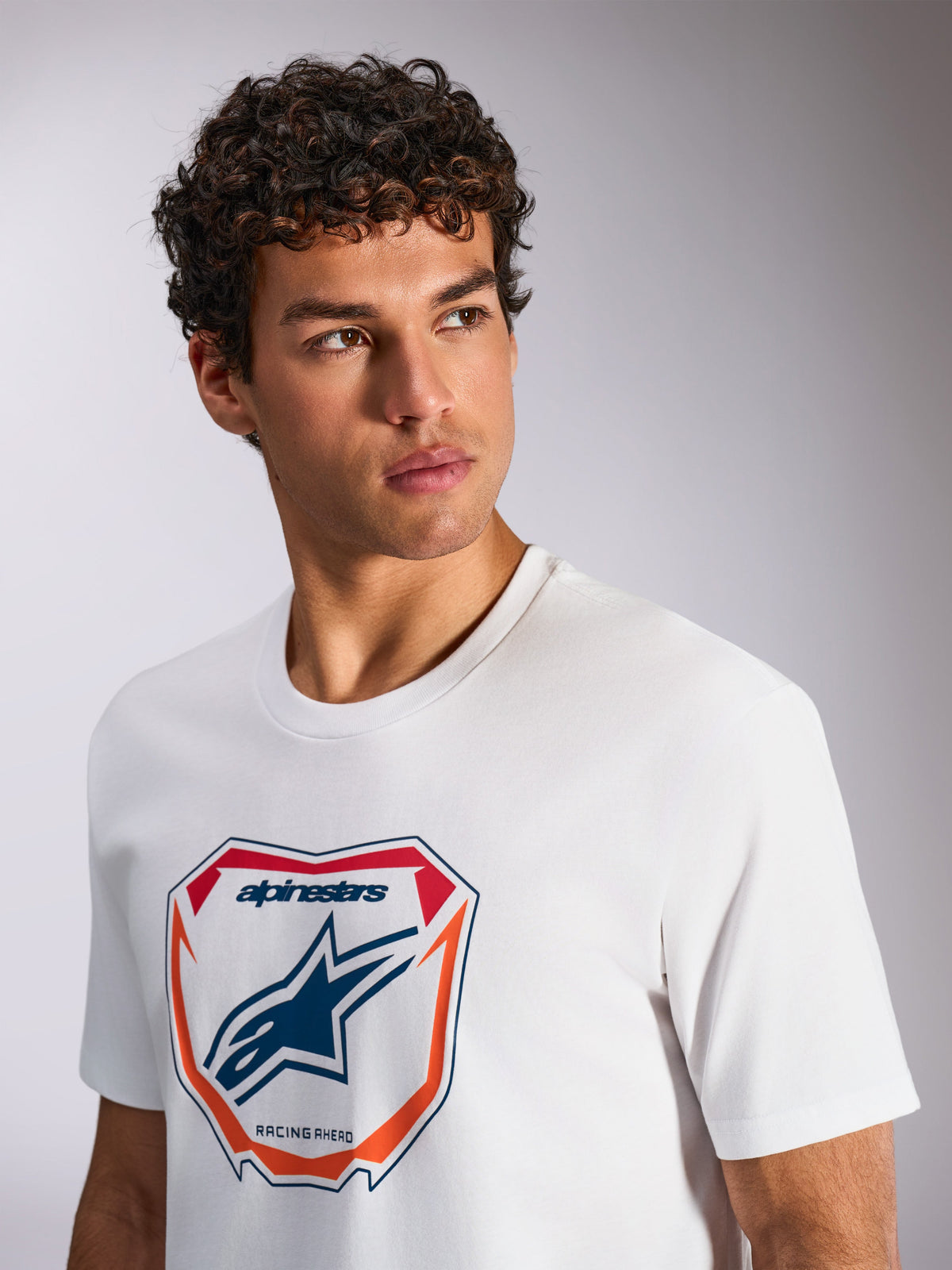 Alpinestars Plate CSF Tee, Short Sleeve T-Shirt, White, featuring a front Astars MX plate graphic with red and orange accents, 'Racing Ahead' text, worn by a model, casual motorsport streetwear