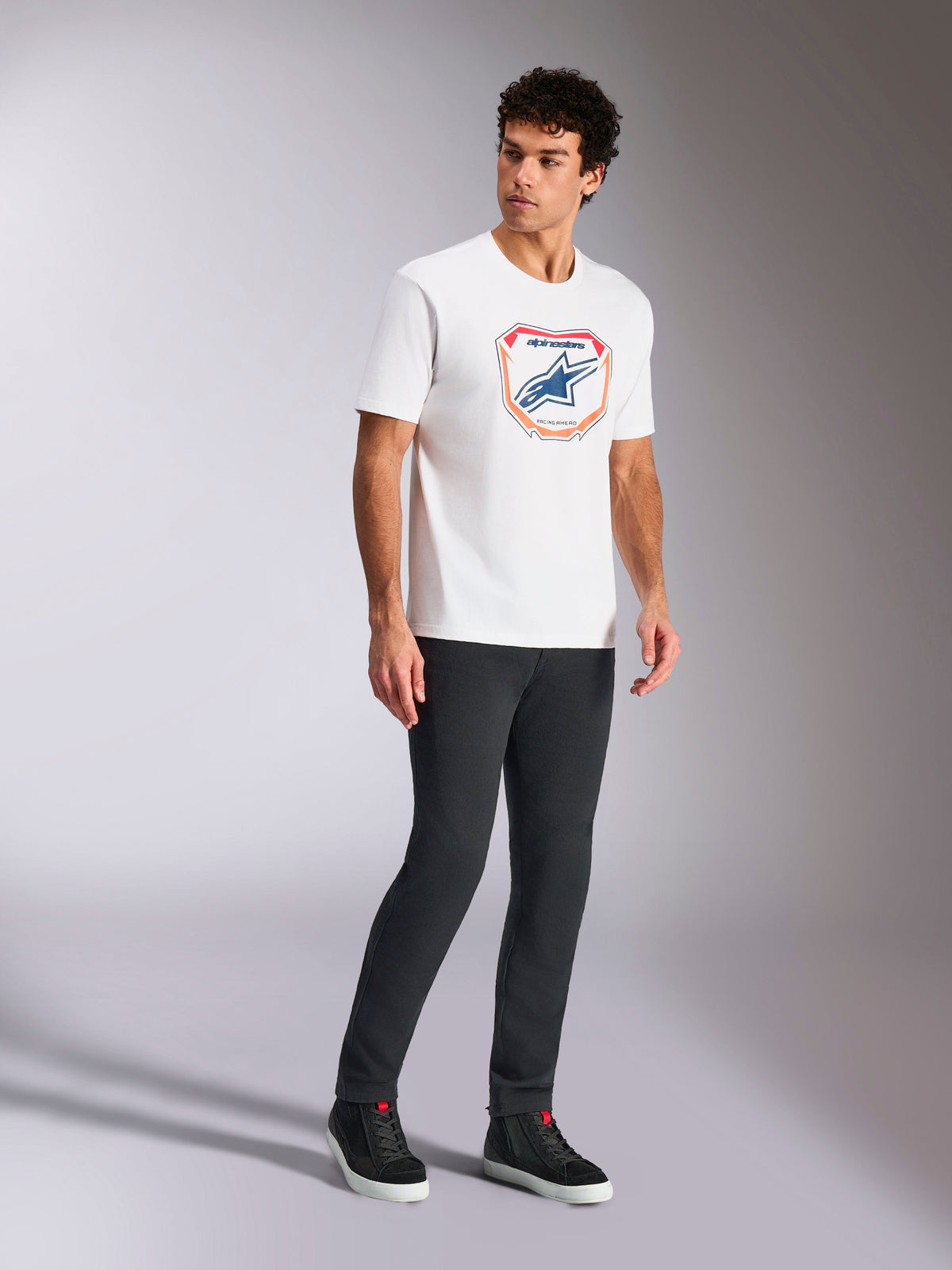Alpinestars Plate CSF Tee, Short Sleeve T-Shirt, White, featuring a front Astars MX plate graphic in blue and orange, casual motorsport-inspired streetwear worn with dark pants and high-top sneakers