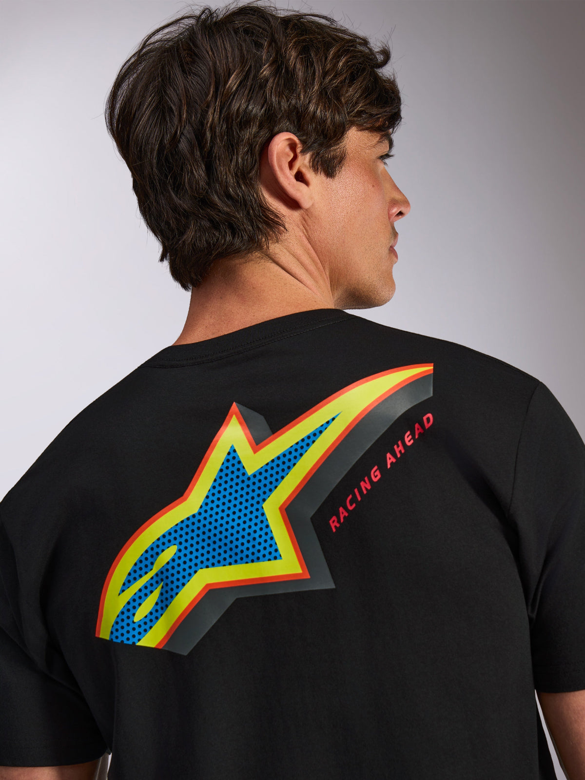 Alpinestars Angler CSF Tee, Short Sleeve T-Shirt, Black, Large Multi-Color Astars Logo on Back with Blue Perforated Fill, Yellow and Red Outlines, and 'RACING AHEAD' Text, Casual Motorsport Streetwear