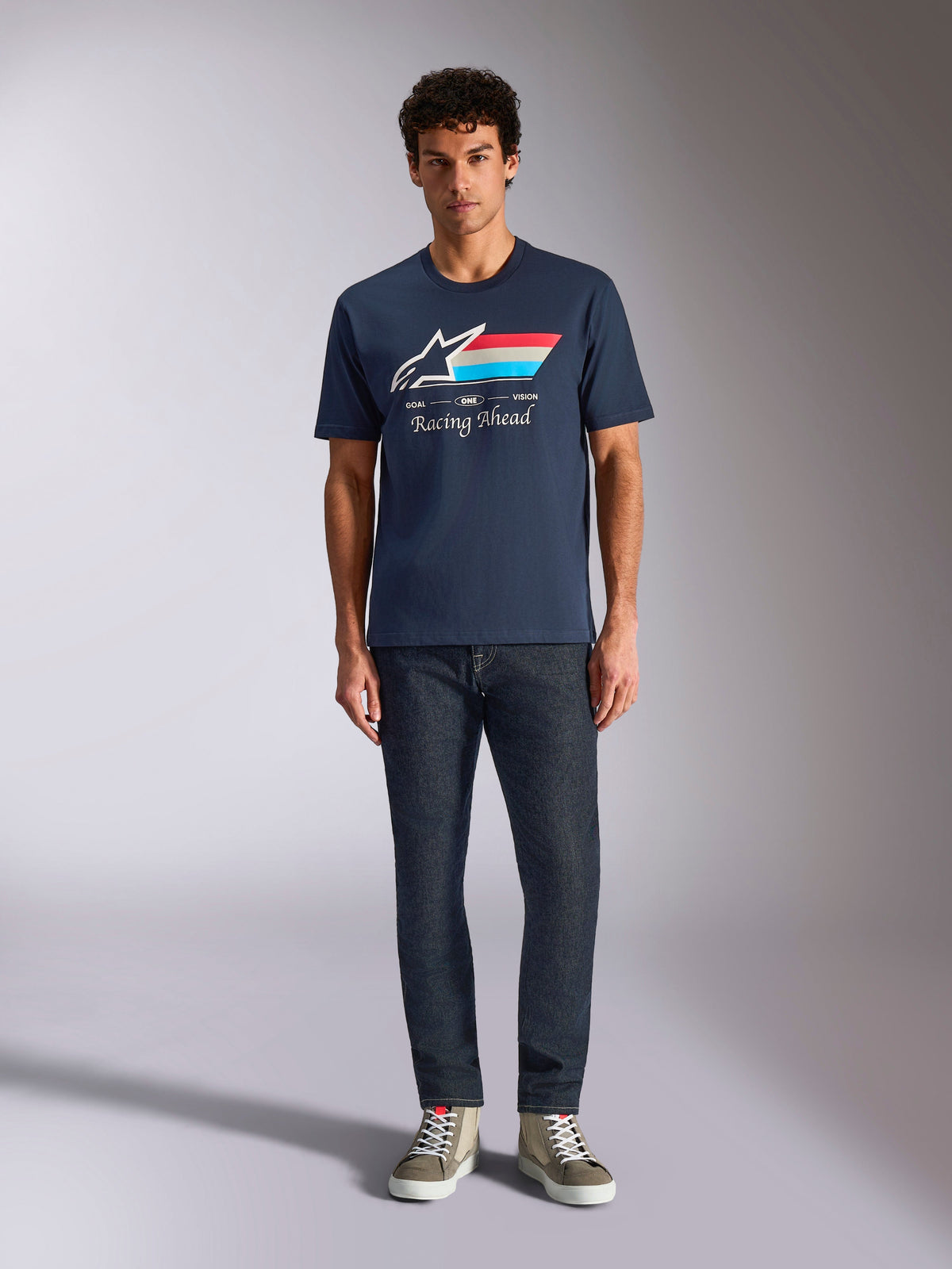 Alpinestars Trifecta CSF Tee, Short Sleeve T-Shirt, Navy Blue, White Astars Logo with Red White and Light Blue Stripes and 'Racing Ahead' text, worn with dark jeans and olive sneakers, Casual Motorsport Streetwear