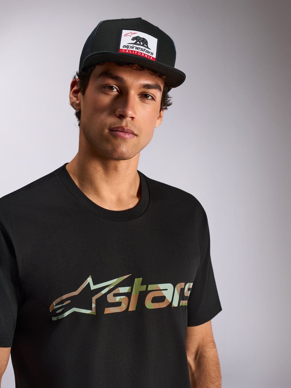 Alpinestars Verdure Camo CSF Tee, Short Sleeve T-Shirt, Black, Camo Fill Astars Logo, worn by male model with black Alpinestars California trucker hat, casual motorsport streetwear