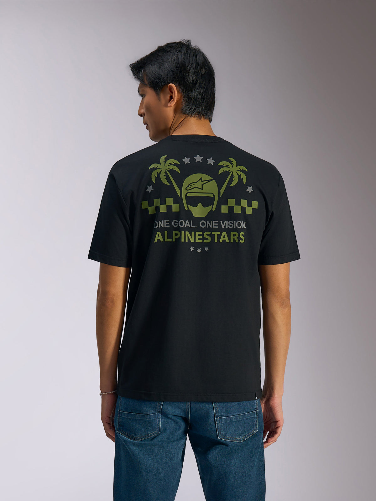 Alpinestars Order CSF Tee, Short Sleeve T-Shirt, Black, Back View, Olive Green Graphic with Palm Trees and Helmet Logo, 'ONE GOAL. ONE VISION. ALPINESTARS' text, paired with blue jeans, casual motorsport streetwear