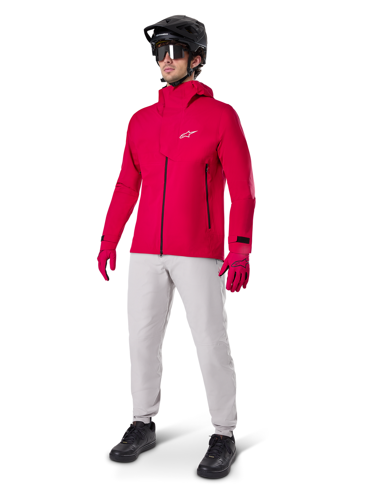 Male cyclist wearing the Alpinestars A-Dura Elite Waterproof Jacket in Red Fluo, paired with light grey technical pants, red gloves, black MTB helmet with goggles, and black shoes, complete high-performance outfit for mountain biking