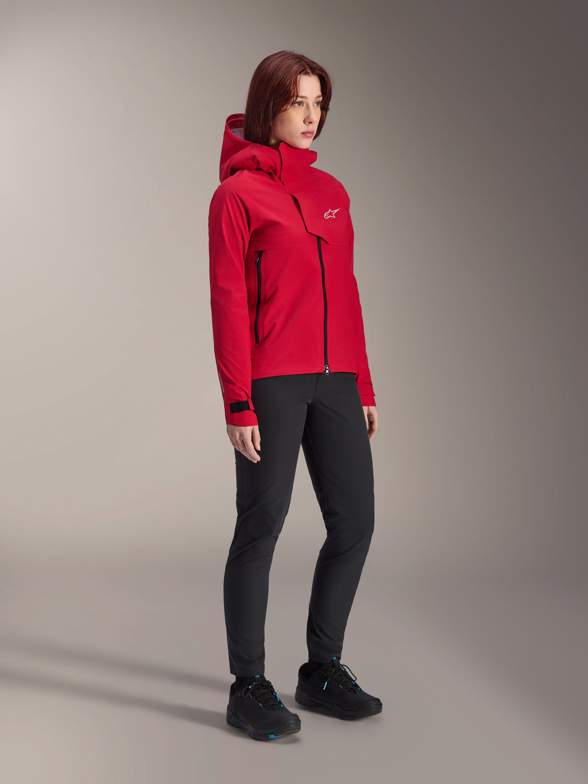 Alpinestars Woman Stella A-Dura Elite Waterproof Jacket, Red Fluo, hooded mountain bike rain jacket with white Astars logo on the chest flap, worn with black pants and black mountain bike shoes, technical performance gear for trail riding