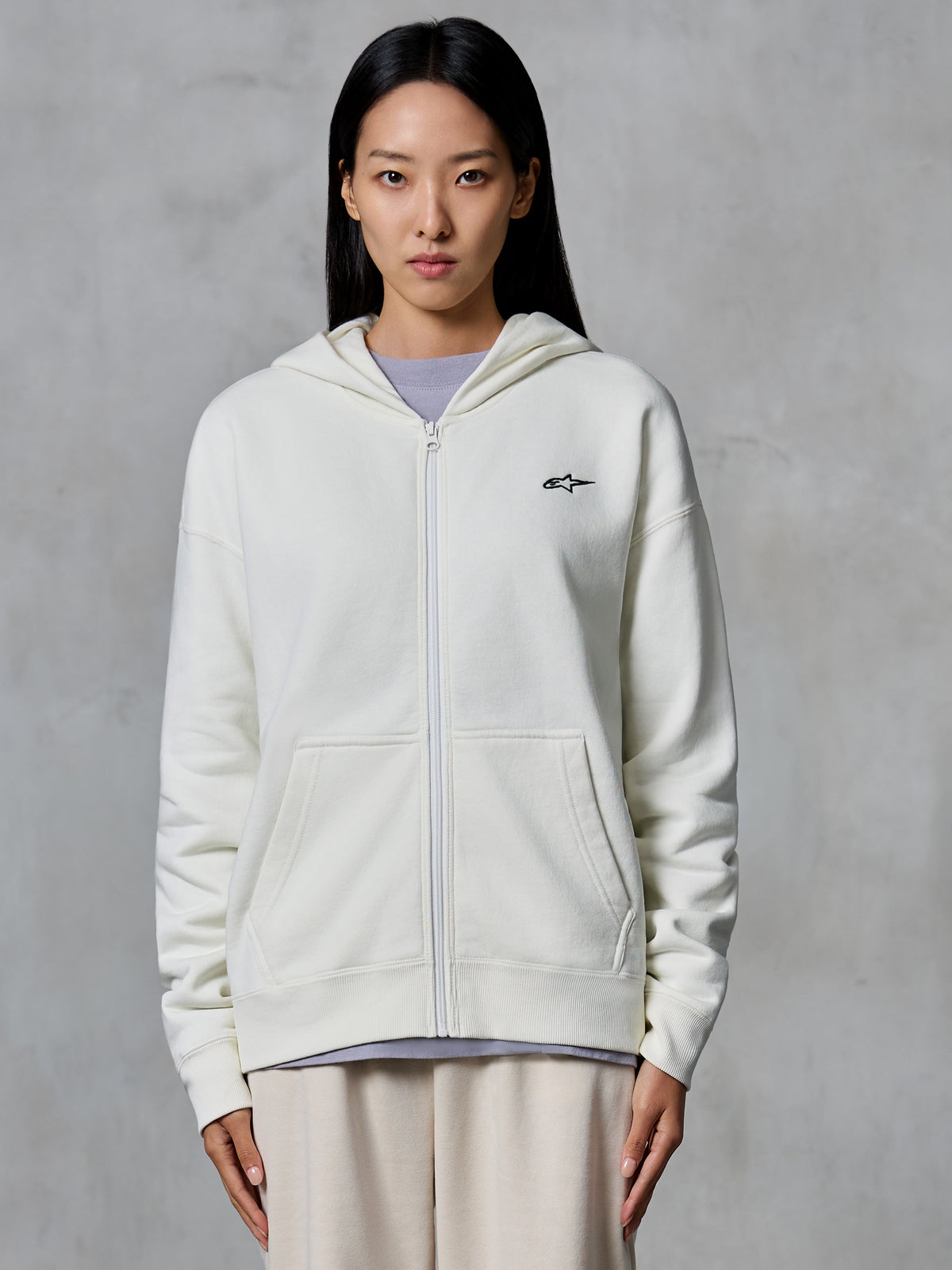 Alpinestars Essentials Ageless Zip Hoodie, Off White, zip-front fleece sweatshirt worn by a model, featuring a small black Astars logo on the chest, relaxed fit, casual motorsport-inspired lifestyle wear