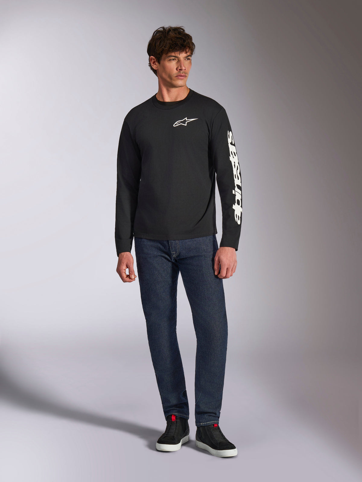 Alpinestars Trackside CSF Tee, Long Sleeve T-Shirt, Black and White, worn with dark blue jeans and black sneakers, featuring white Ride 4.0 logo on the chest and Alpinestars wordmark on the sleeve, casual motorsport-inspired streetwear