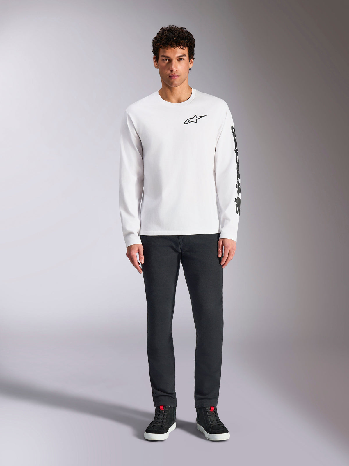 Alpinestars Trackside CSF Tee - Long Sleeve, White with Black branding, small logo on chest and vertical text on sleeve, worn by model with dark pants and black sneakers, casual motorsport-inspired streetwear