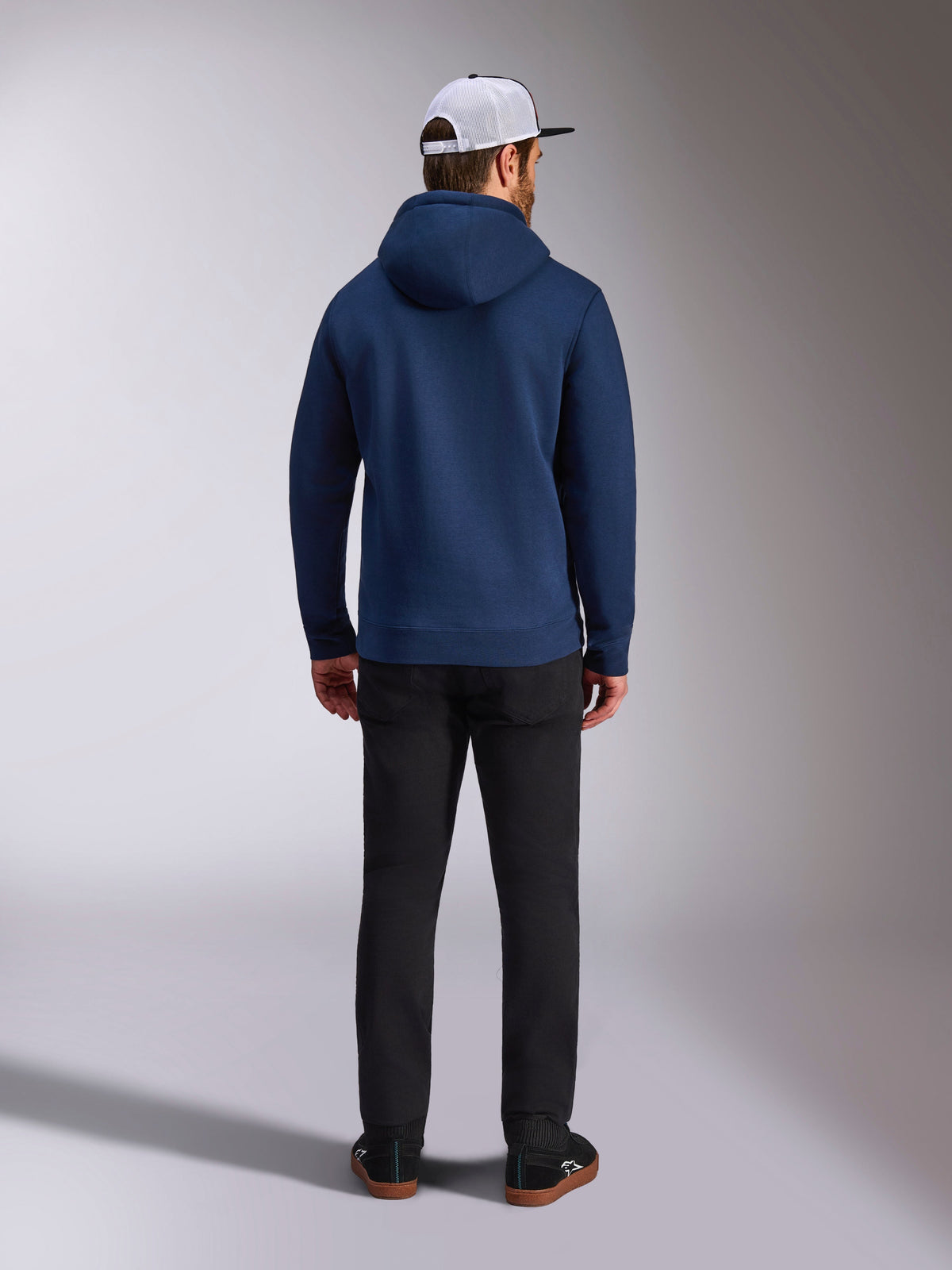Alpinestars Frontal Hoodie, Navy Blue, back view of man wearing casual pullover fleece hoodie, featuring ribbed cuffs and hem, paired with black pants and a white mesh cap, motorsport-inspired streetwear