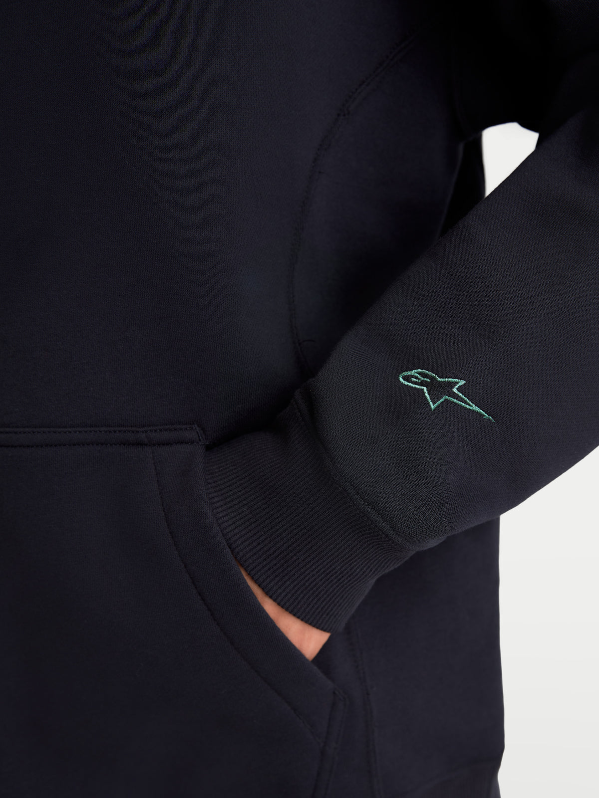 Alpinestars Guise Oversized Crew, Black Sportswear Fleece Pullover, detailed view showing the sleeve with a teal embroidered Astars logo, ribbed cuff, and kangaroo pocket entry, premium cotton and recycled polyester blend sweatshirt.