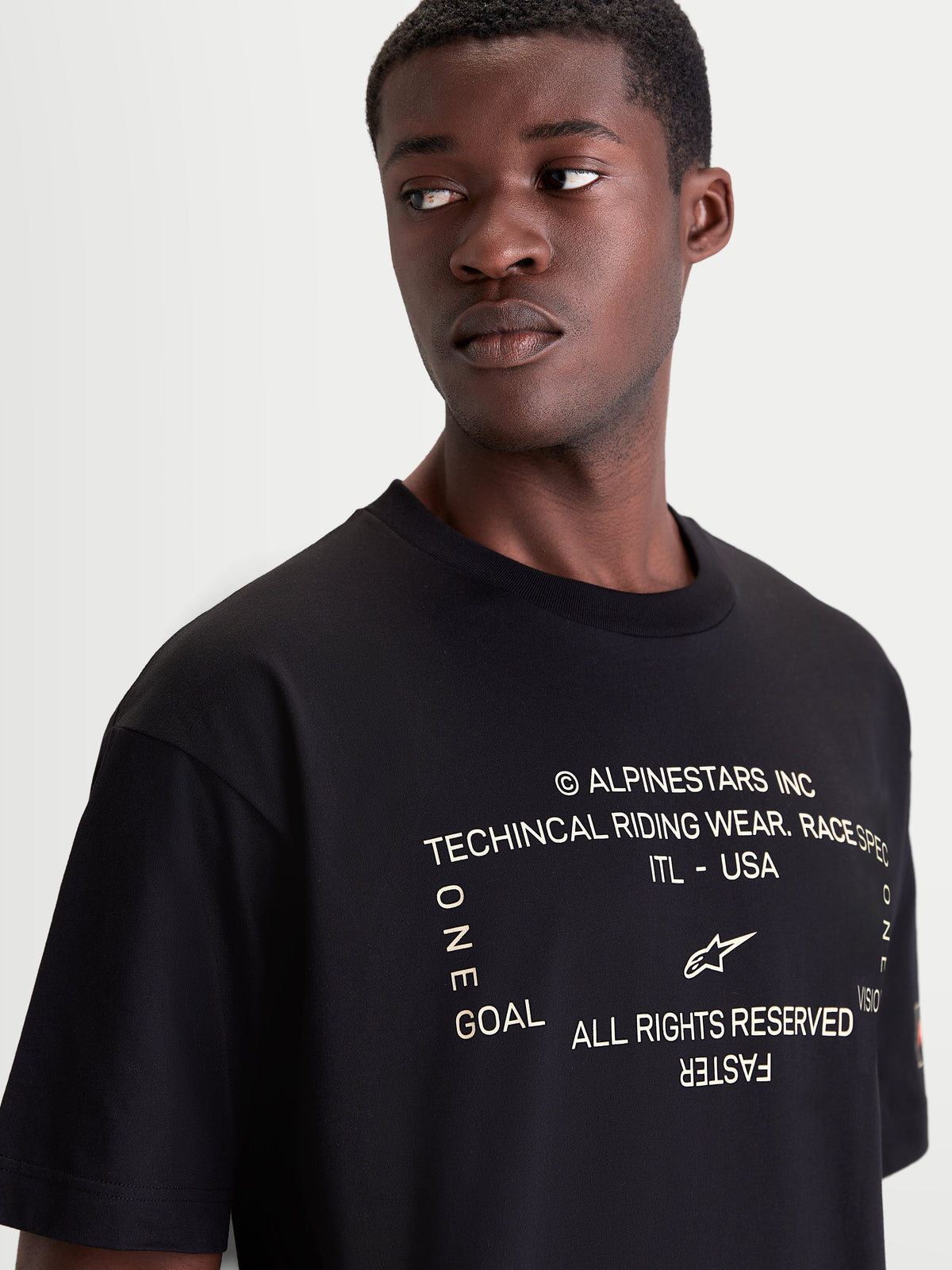 Alpinestars Infinity Oversized CSF Tee, Men's Short Sleeve Sportswear T-shirt, Black, featuring a soft-hand front chest graphic with Alpinestars branding and motorsport-inspired text, close-up on model for a premium off-bike look.