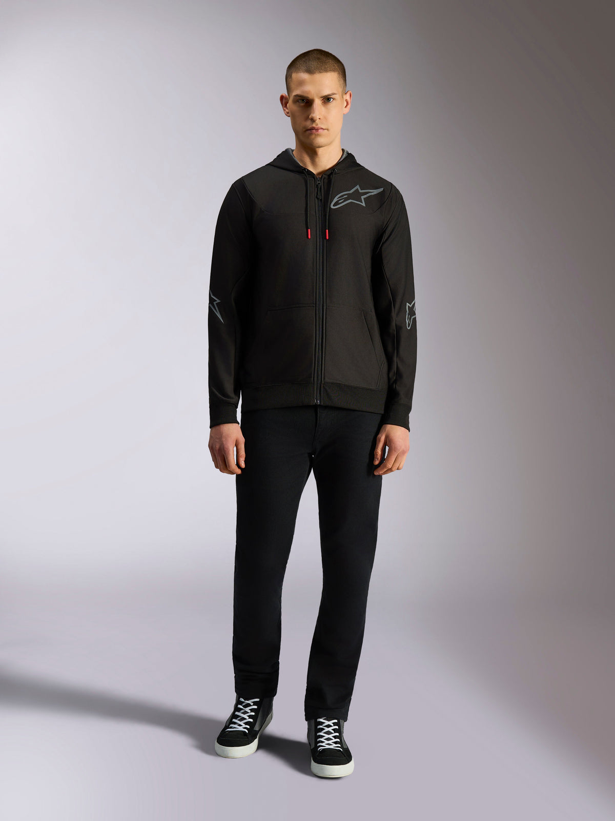 Alpinestars Sessions V3 Hoodie, black full-zip hoodie with grey Astars chest logo, elbow and forearm graphics, red drawcord accents, worn by male model with black pants and sneakers, casual motorsport apparel