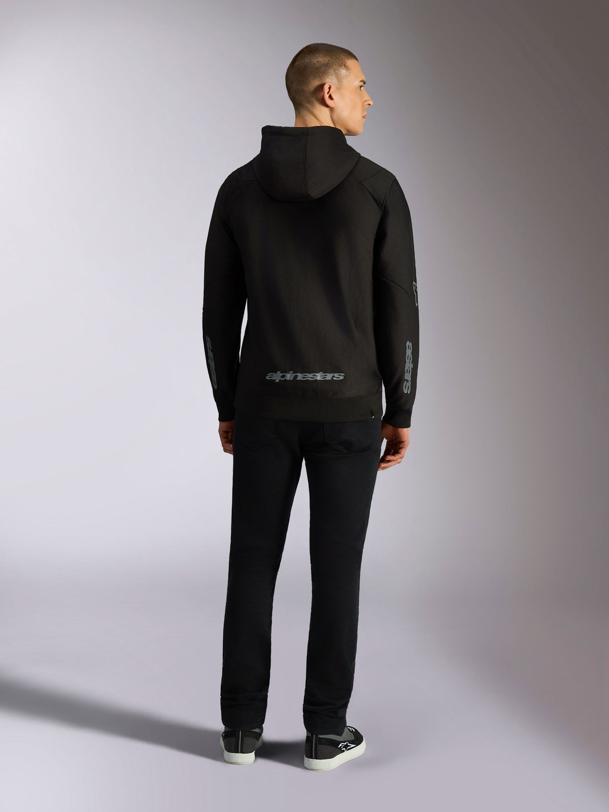 Alpinestars Sessions V3 Hoodie, casual streetwear, black with grey Alpinestars wordmark on the lower back and 'astars' branding on the sleeves, back view of male model wearing hoodie and black pants, modern motorsport-inspired design