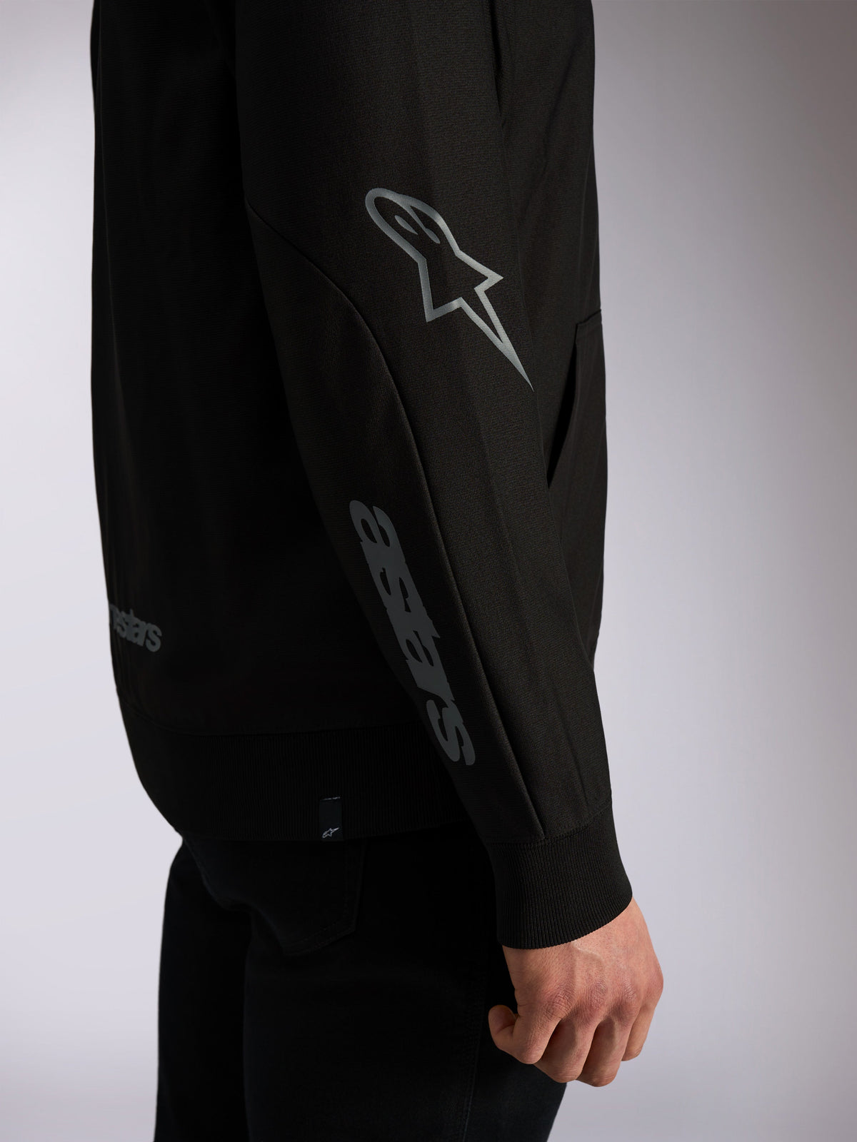 Alpinestars Sessions V3 Hoodie, black casual streetwear, close-up of sleeve featuring grey Astars logo on elbow and wordmark on forearm, ribbed cuffs, motorsport-inspired design