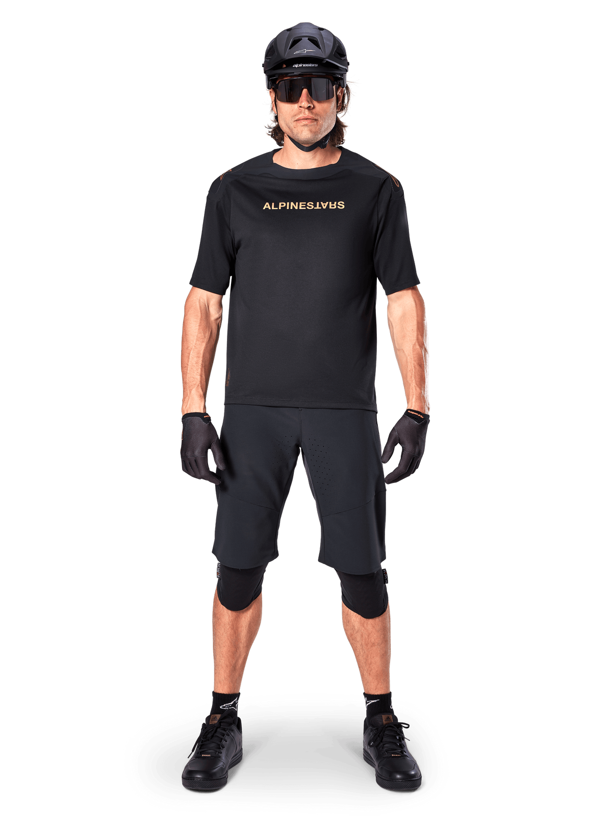 Male mountain bike rider wearing Alpinestars A-Aria Elite Shorts in Black, paired with a matching black Alpinestars short-sleeve jersey, black helmet, gloves, and knee guards, complete off-road cycling gear outfit