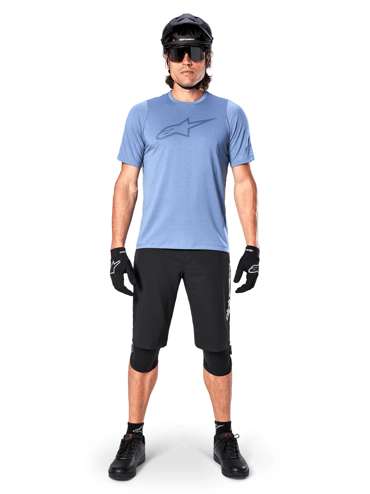 Male mountain bike rider wearing the Alpinestars A-Dura Dri Astar Short Sleeve Jersey in Infinity Blue, featuring a prominent Astars logo on the chest, coordinated with black MTB shorts, black helmet, sunglasses, and protective gear for off-road riding