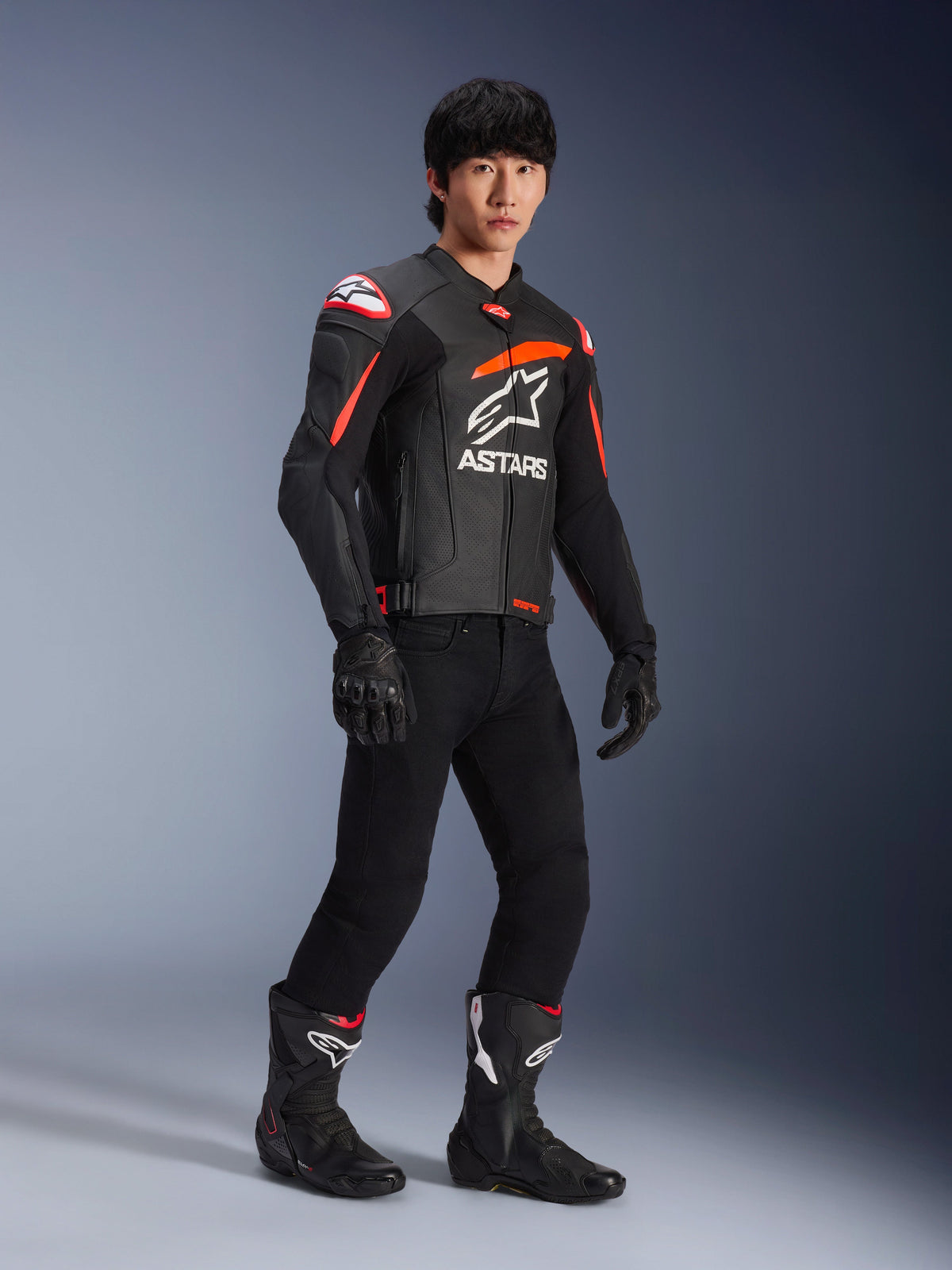 Male rider wearing Alpinestars GP Plus R V4 Airflow Leather Jacket, Black with Red Fluo and White accents, featuring perforated leather and ASTARS chest logo, worn with black riding pants and black motorcycle boots, sport performance gear