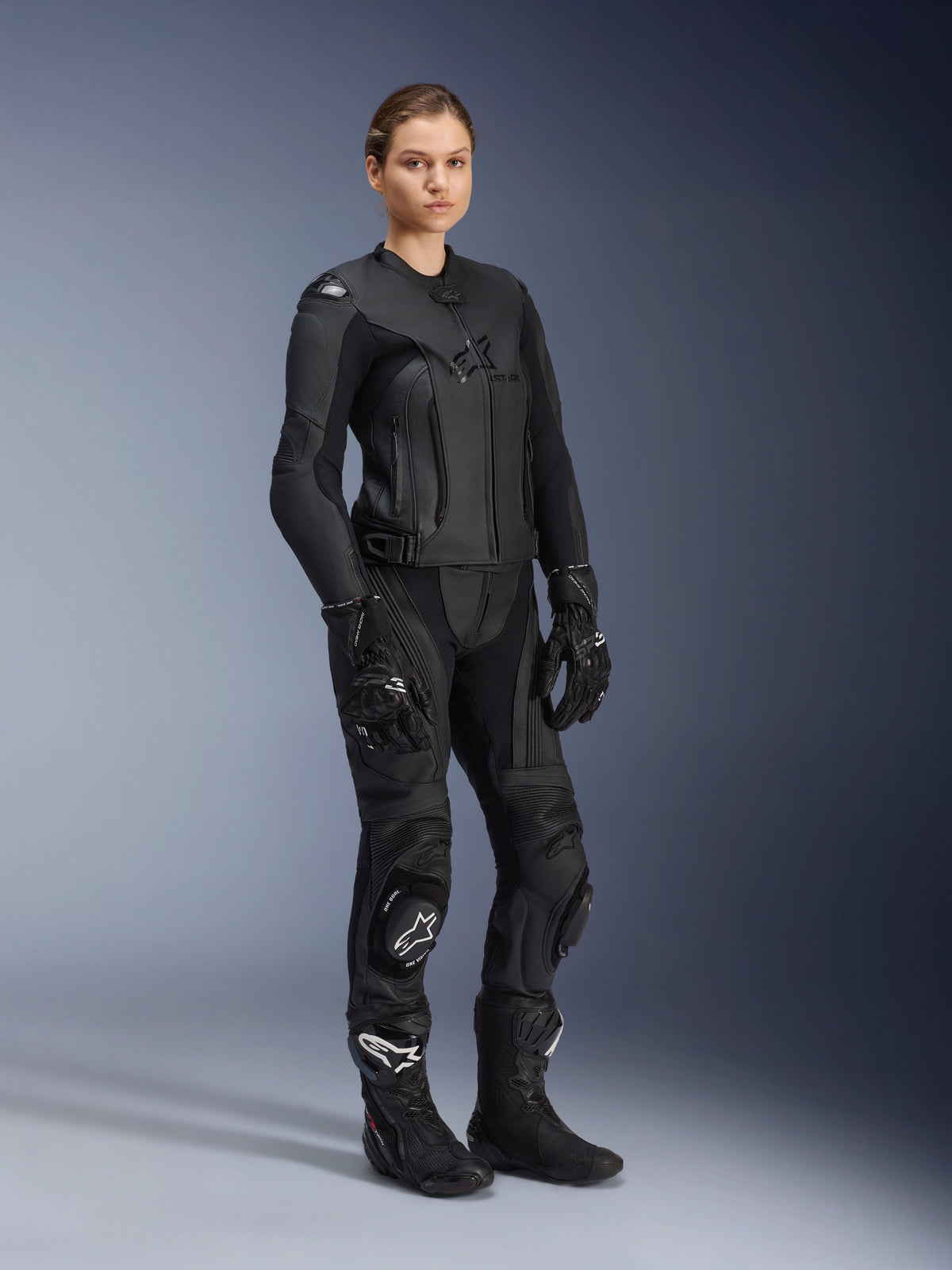 Female rider wearing the Alpinestars Women Stella GP Plus V4 Leather Jacket in Black Black, styled as a complete leather racing suit with matching motorcycle pants, gloves, and boots, featuring a sleek performance design with integrated protection.