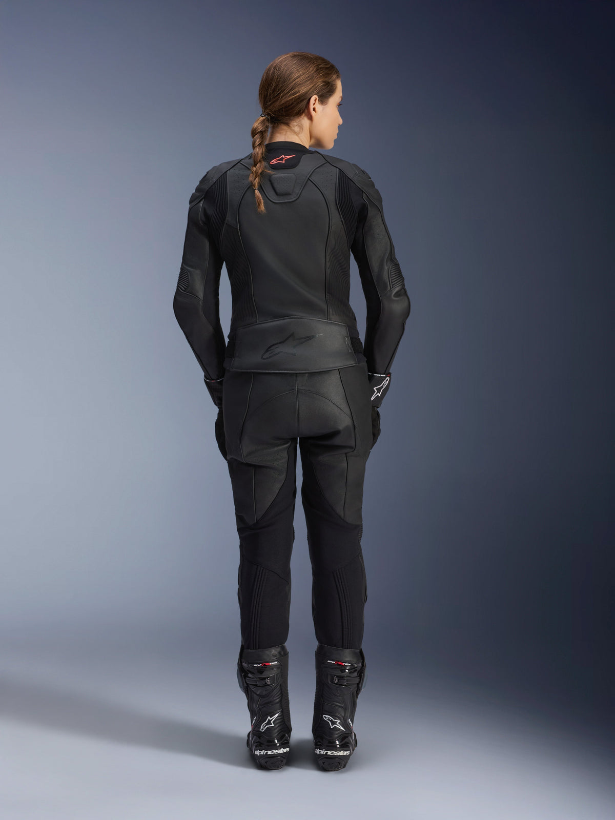 Alpinestars Women Stella GP Plus V4 Leather Jacket, Black Black, full-body rear view of a female rider wearing matching leather pants and boots, sleek minimalist design with a small red logo on the neck, tailored sport silhouette for women