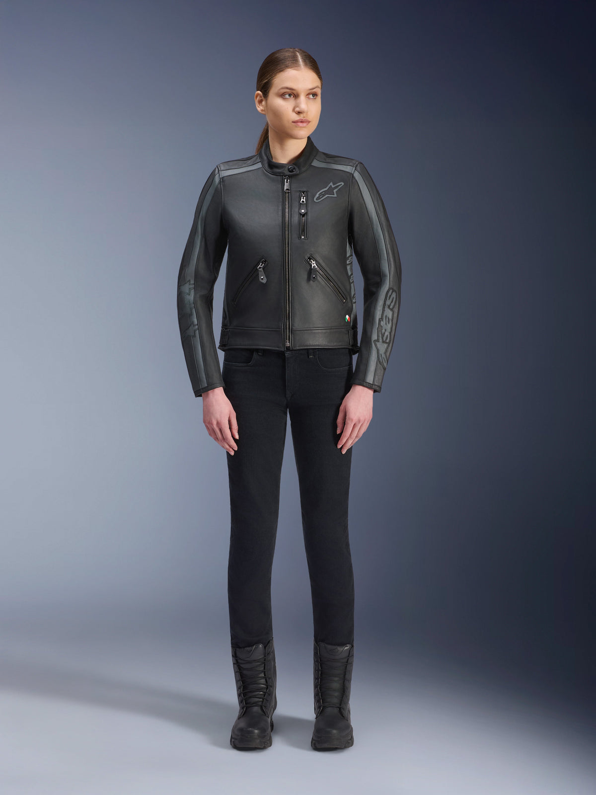 Alpinestars Stella Dyno Leather Jacket, Women's Motorcycle Jacket, Black Tar Gray Dark Gray, full-body studio view of a model wearing the jacket with black slim-fit pants and black boots, featuring bovine leather construction with gray accents and subtle Alpinestars branding on the chest and sleeves.