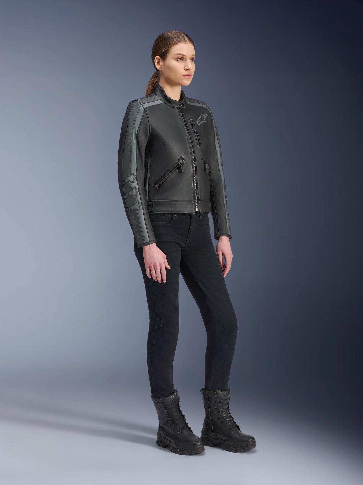Alpinestars Stella Dyno Leather Jacket, Women's Motorcycle Jacket, Black Tar Gray and Dark Gray, worn with black riding pants and boots, featuring grey racing stripes on sleeves and heritage leather design