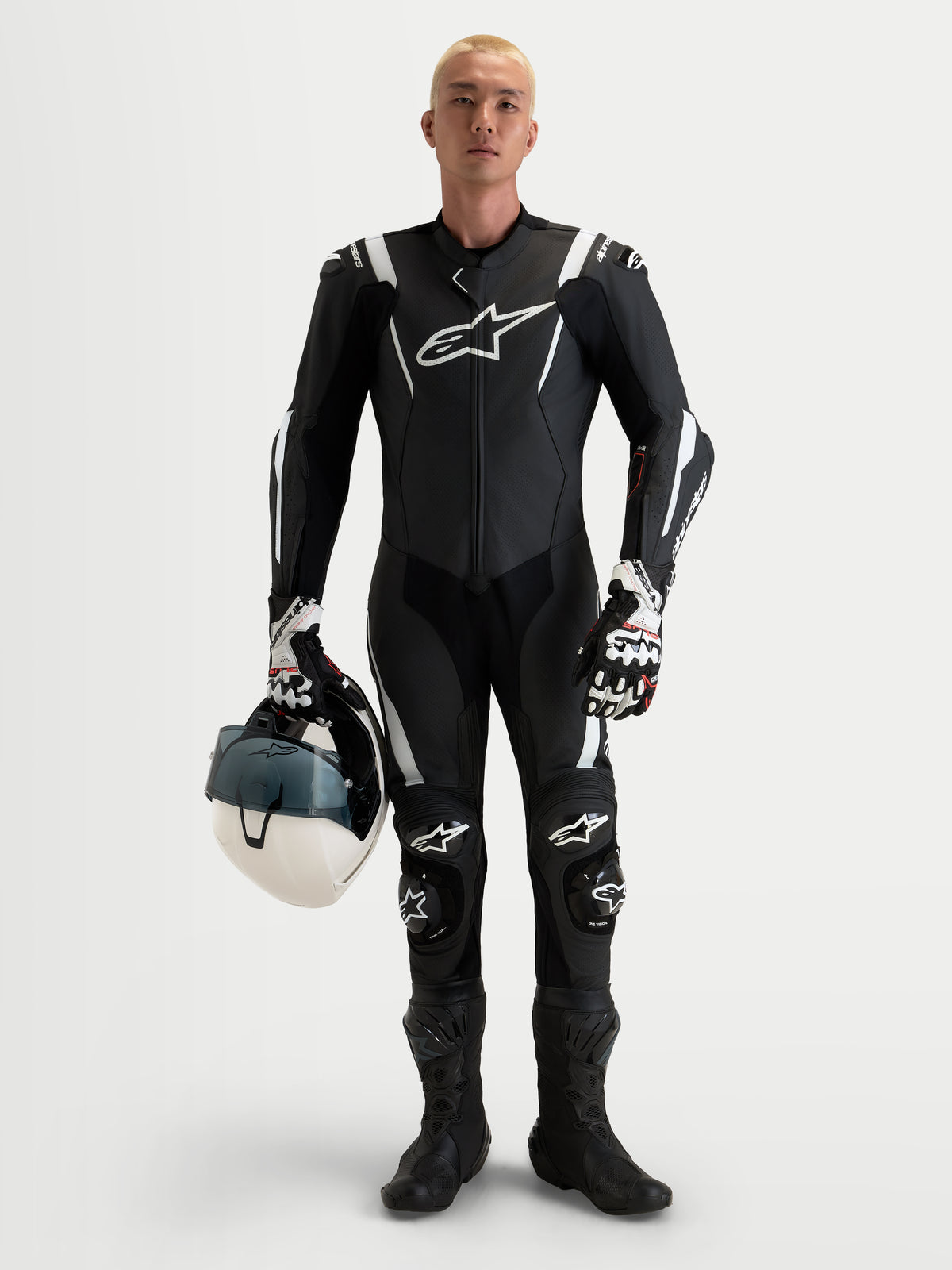 Alpinestars Missile V3 Leather Suit 1 Piece, men's black and white AAA-rated racing leather suit featuring integrated shoulder, elbow, and knee armor, holding a matching white helmet