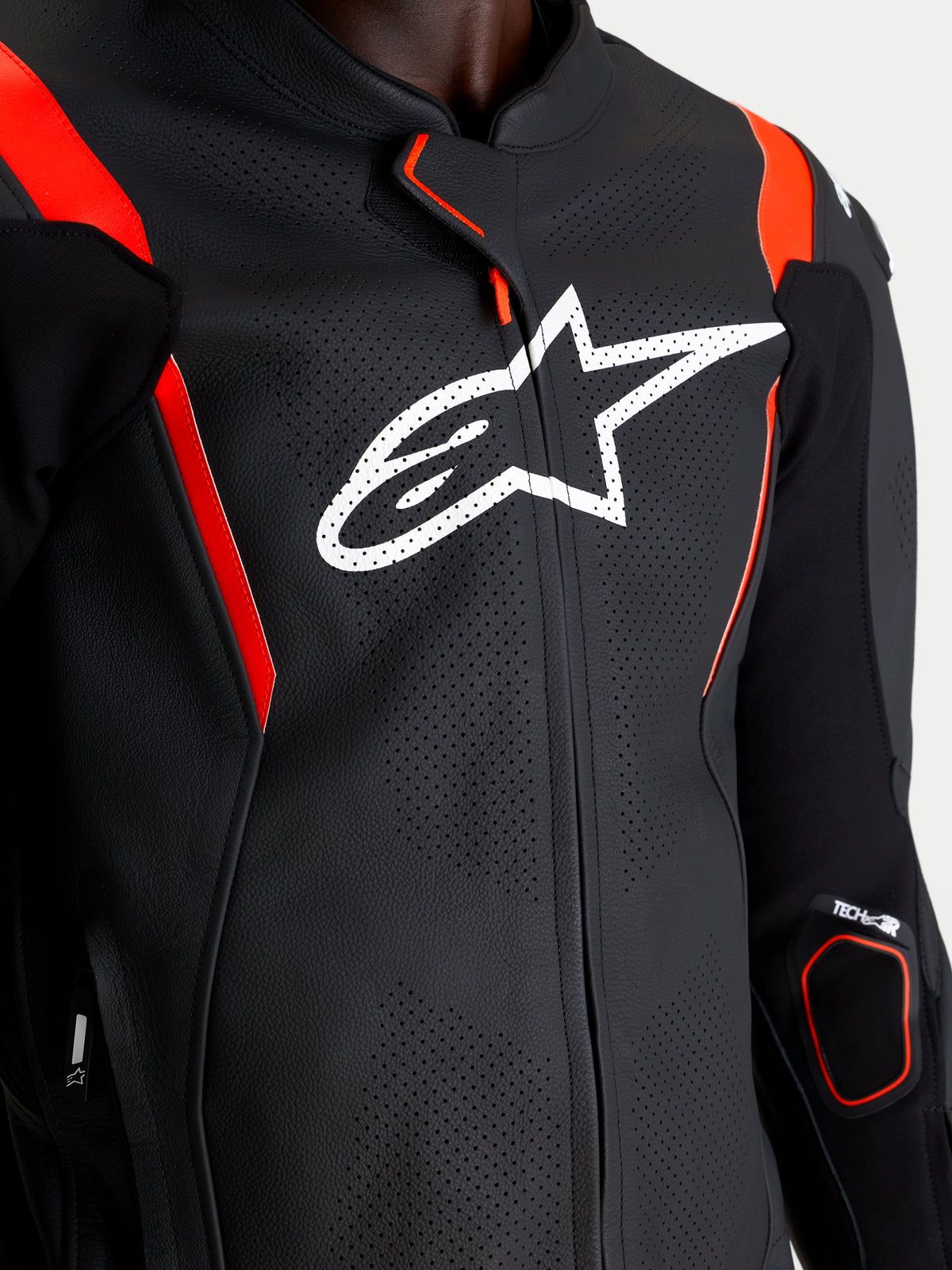 Alpinestars Missile V3 Leather Suit 2 Piece, Black and Red Fluo, close-up of the upper chest featuring white Alpinestars logo, perforated race leather construction, and protective armor details