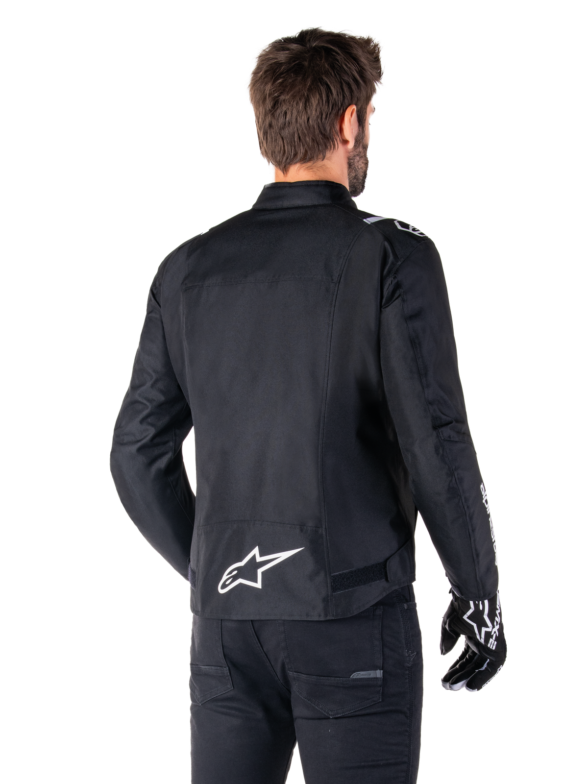 Alpinestars T-SPS V2 Waterproof Jacket, Black and White, rear view of a male rider wearing the jacket, white Alpinestars logo on the lower back, sport cut textile construction, worn with black riding pants and gloves