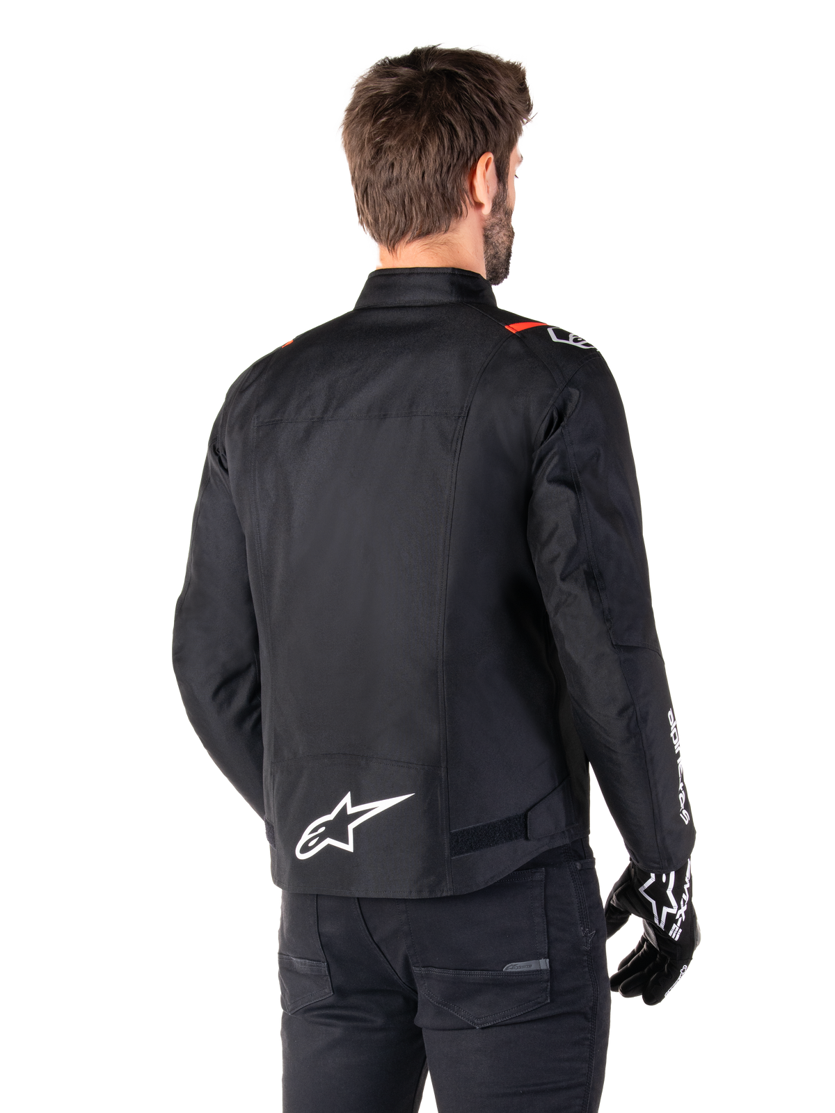 Alpinestars T-SPS V2 Waterproof Jacket, Black White Red Fluo, rear view, featuring white Alpinestars logo on the lower back and red accents on the shoulders, worn with black riding gloves and pants, sport-style textile motorcycle jacket.