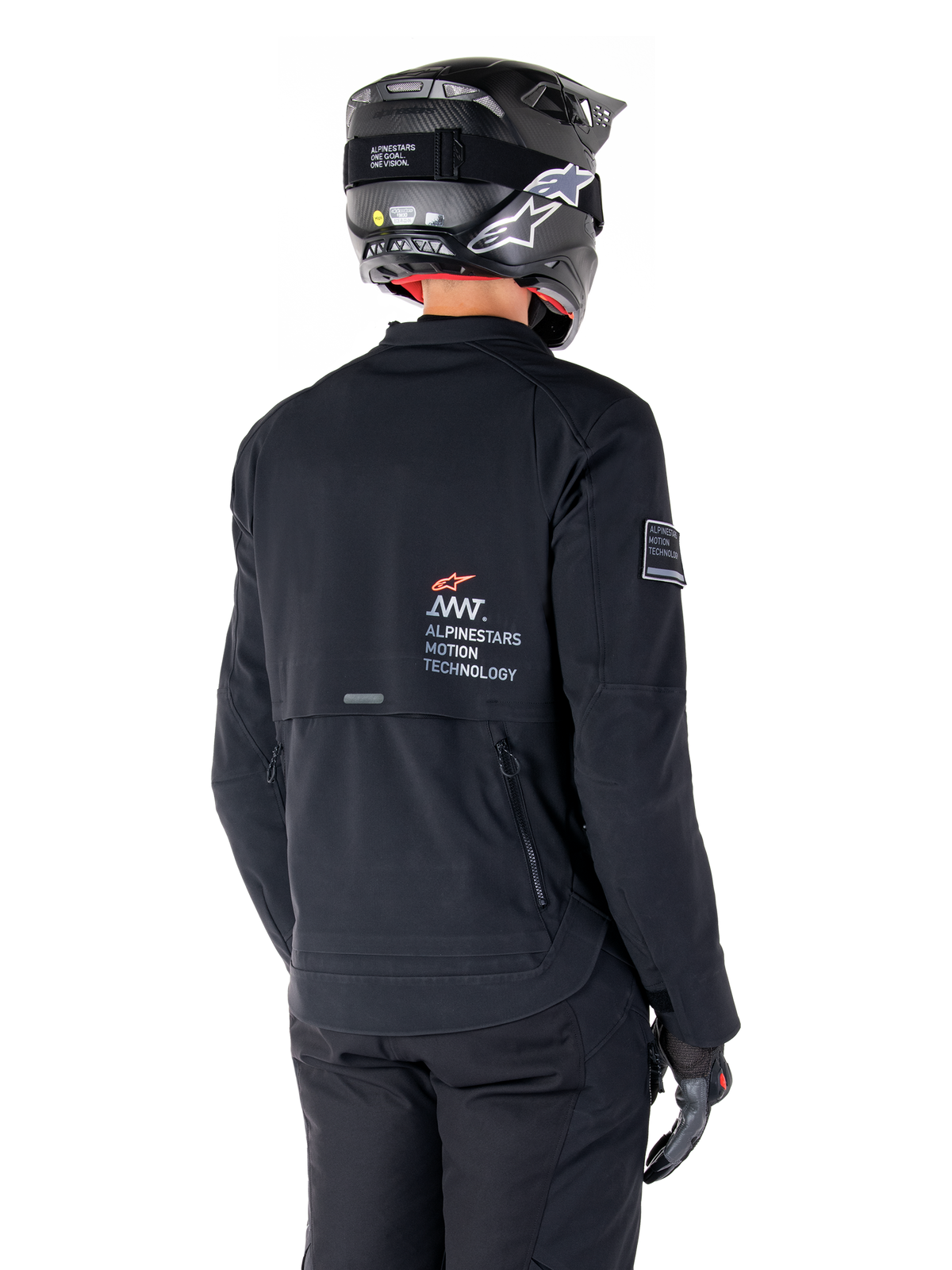 Rear view of a rider wearing the Alpinestars AMT-8 Stretch Drystar® XF Jacket in Black, featuring 'AMT Alpinestars Motion Technology' branding on the back, technical zippered ventilation, paired with a black motorcycle helmet and gloves
