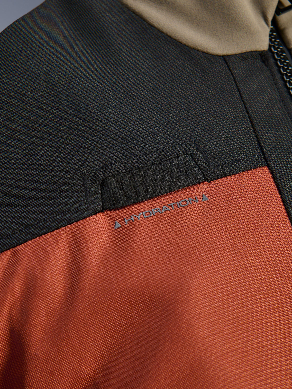 Close-up detail of the Alpinestars Andes V4 Drystar® Jacket in Walnut Rust Black, highlighting the integrated chest hydration hose loop and durable ripstop textile construction.