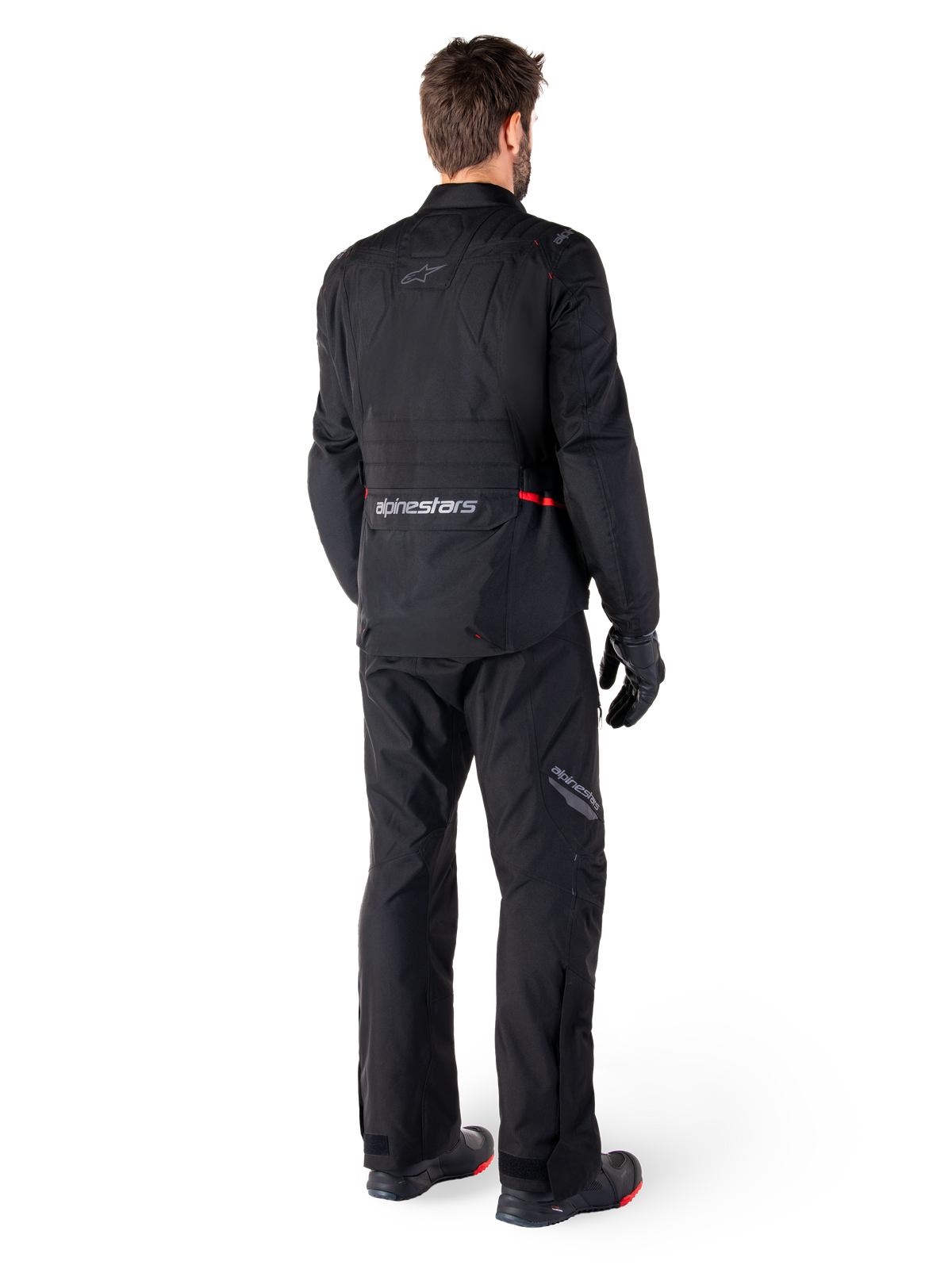 Rear view of a rider wearing the Alpinestars ST-1 Waterproof Jacket and matching pants in black, featuring subtle red accents, a large lower back cargo pocket with branding, and a streamlined adventure touring design.