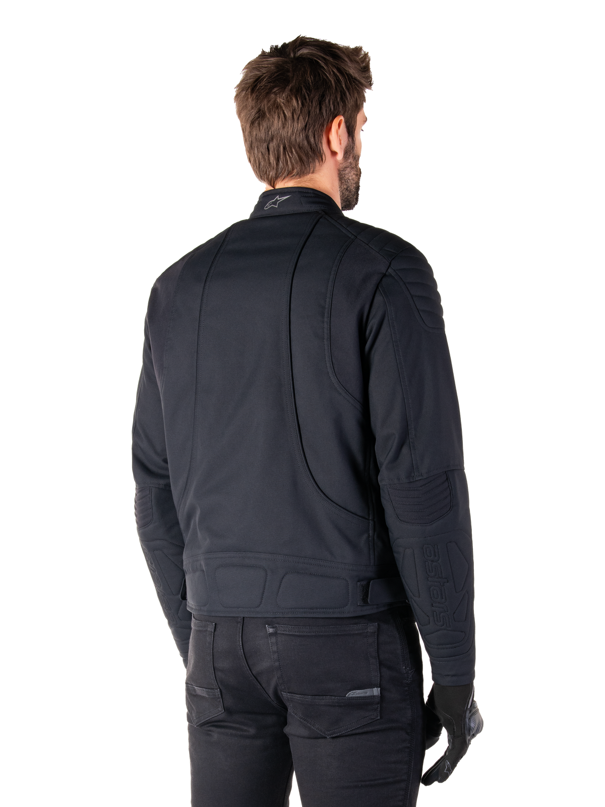 Alpinestars Clayton WR Jacket in Black, rear three-quarter view on a male model, urban motorcycle jacket with quilted padding on shoulders and elbows, technical stitch lines, and reflective logo on the collar, styled with black pants and gloves.