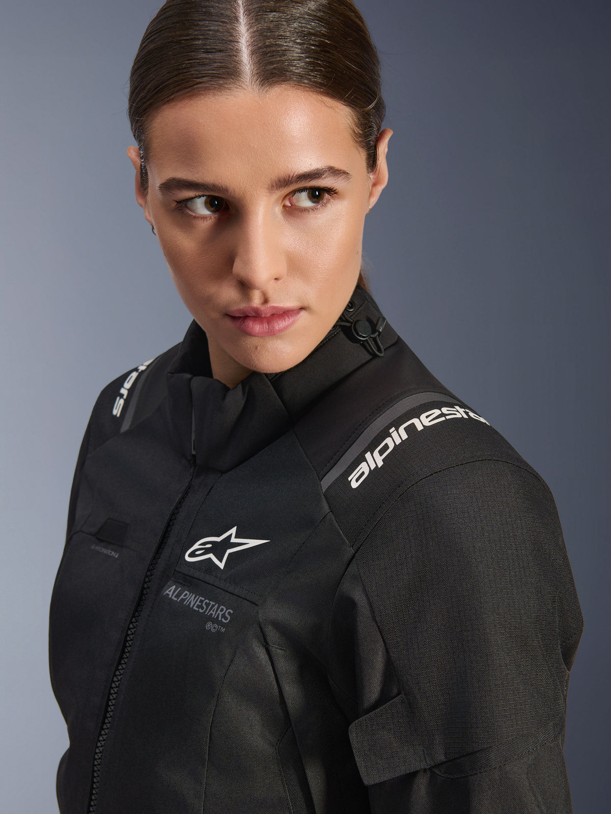 Alpinestars Woman Stella Andes V4 Drystar® Jacket, Black motorcycle jacket, close-up studio portrait showing the upper torso and shoulder, featuring white Alpinestars logos, high-quality textile material, and a sleek feminine fit