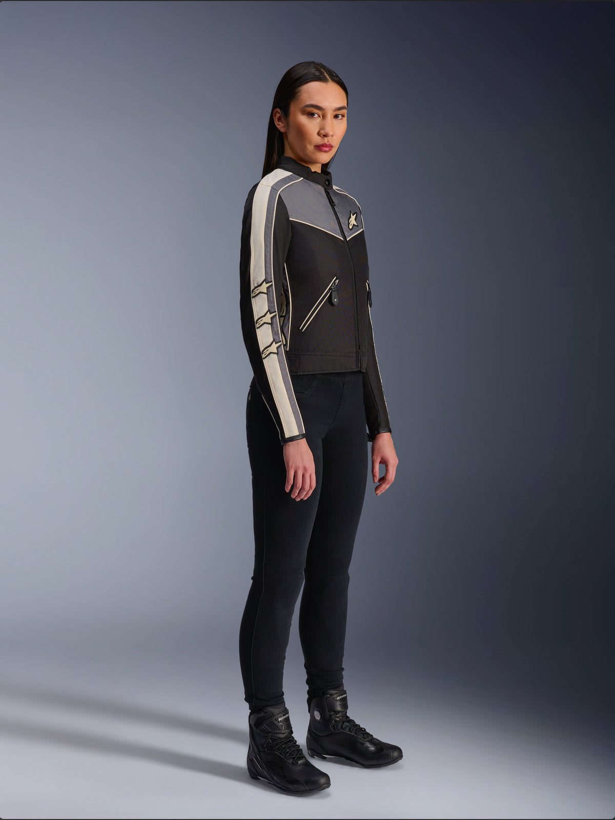 Alpinestars Stella T-Dyno WR Jacket, Women's textile motorcycle jacket, Black, Dark Gray, and Ecru, featuring vintage-inspired design with cream sleeve stripes and star logos, worn with black pants and riding boots, heritage-inspired urban riding gear