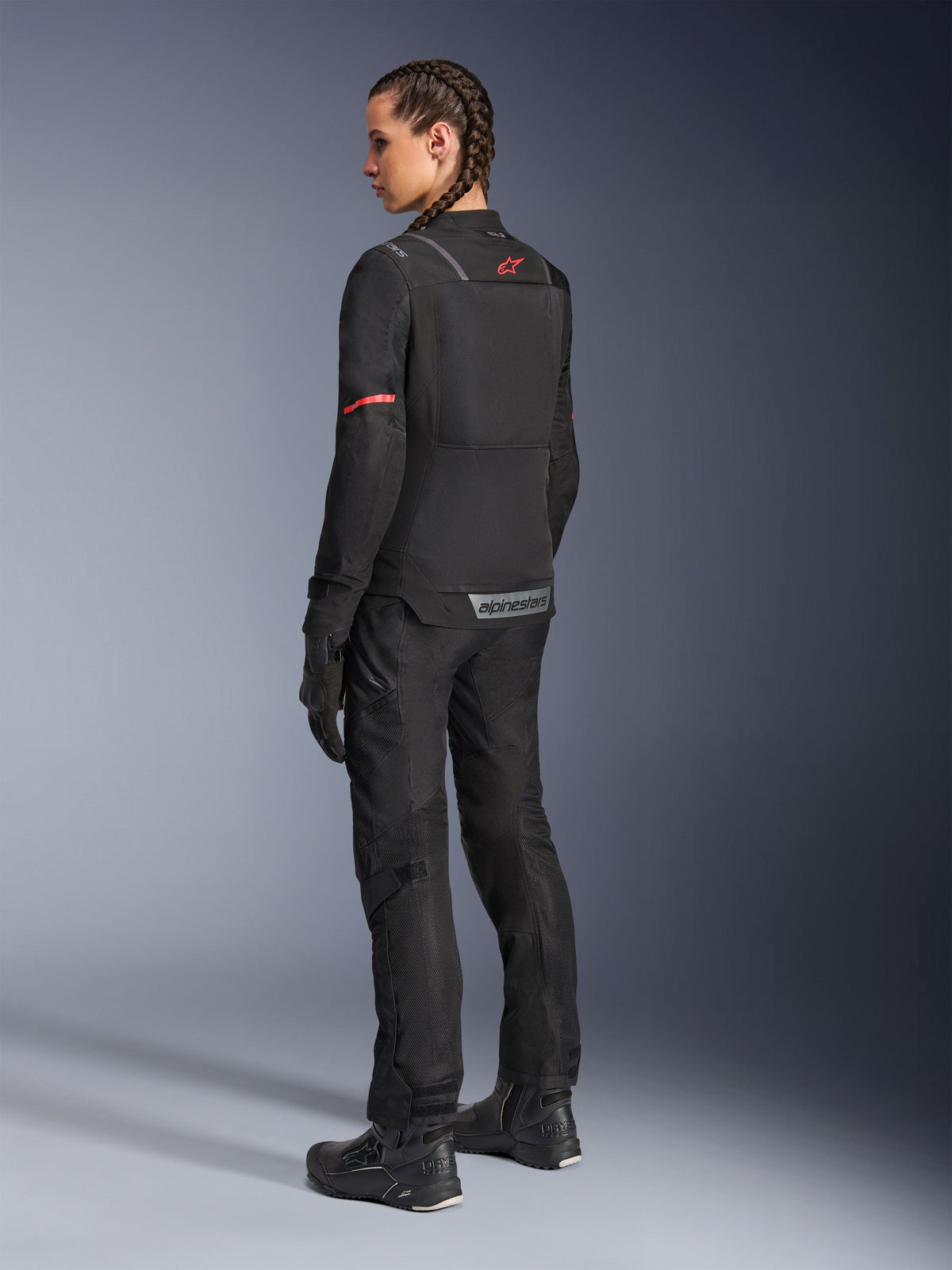 Female rider wearing black Alpinestars Stella Andes Air Drystar® Pants and matching Stella ST-2 Air Jacket, rear view showing technical textile construction and mesh panels, red star logo on the jacket back, paired with black riding boots and gloves.