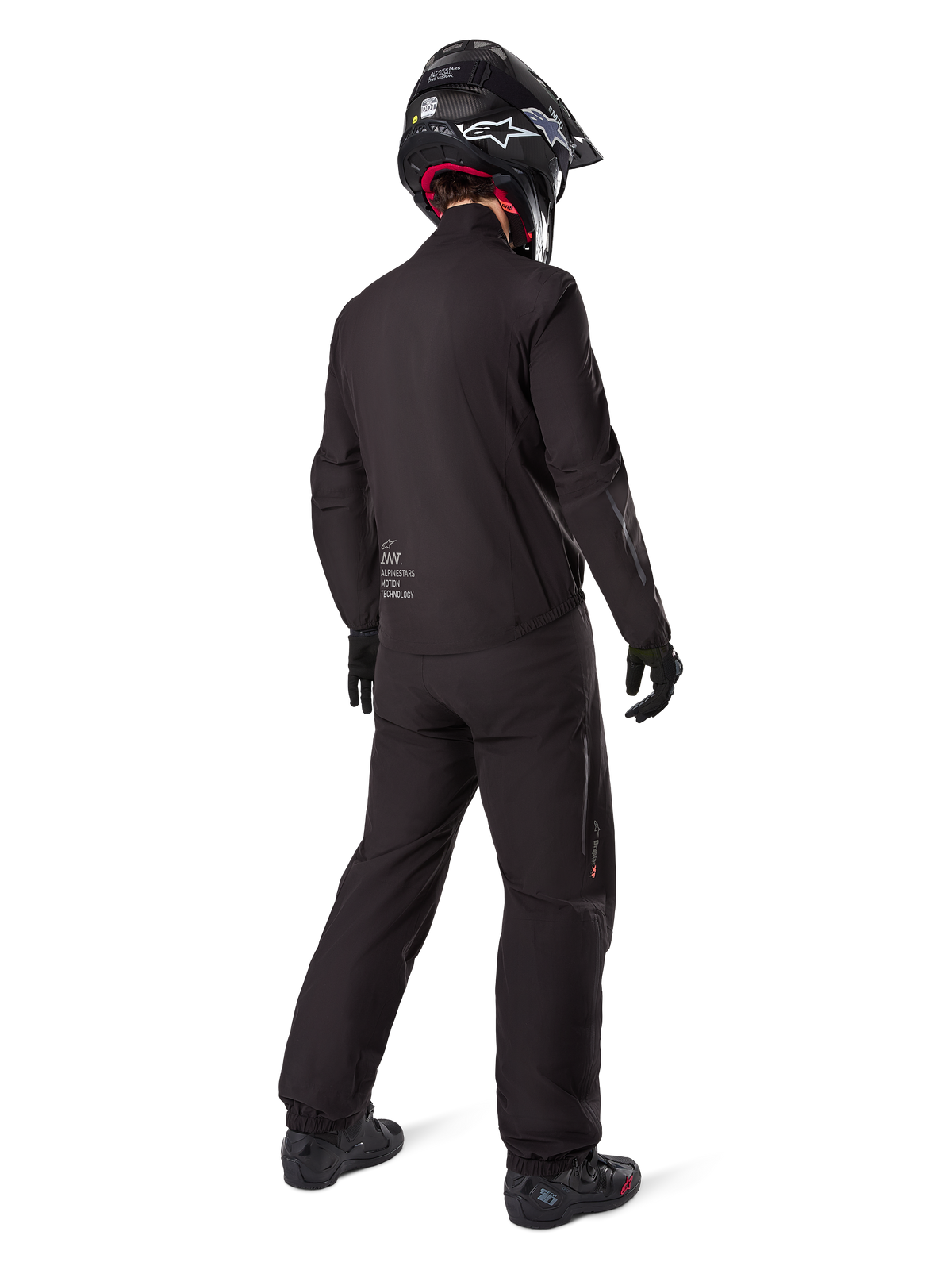 Motorcycle rider seen from behind wearing the black Amt-8 Stretch Drystar® XF Pants and matching jacket, complete adventure touring outfit with black helmet and boots, technical waterproof and stretchable gear for long-range motorcycling