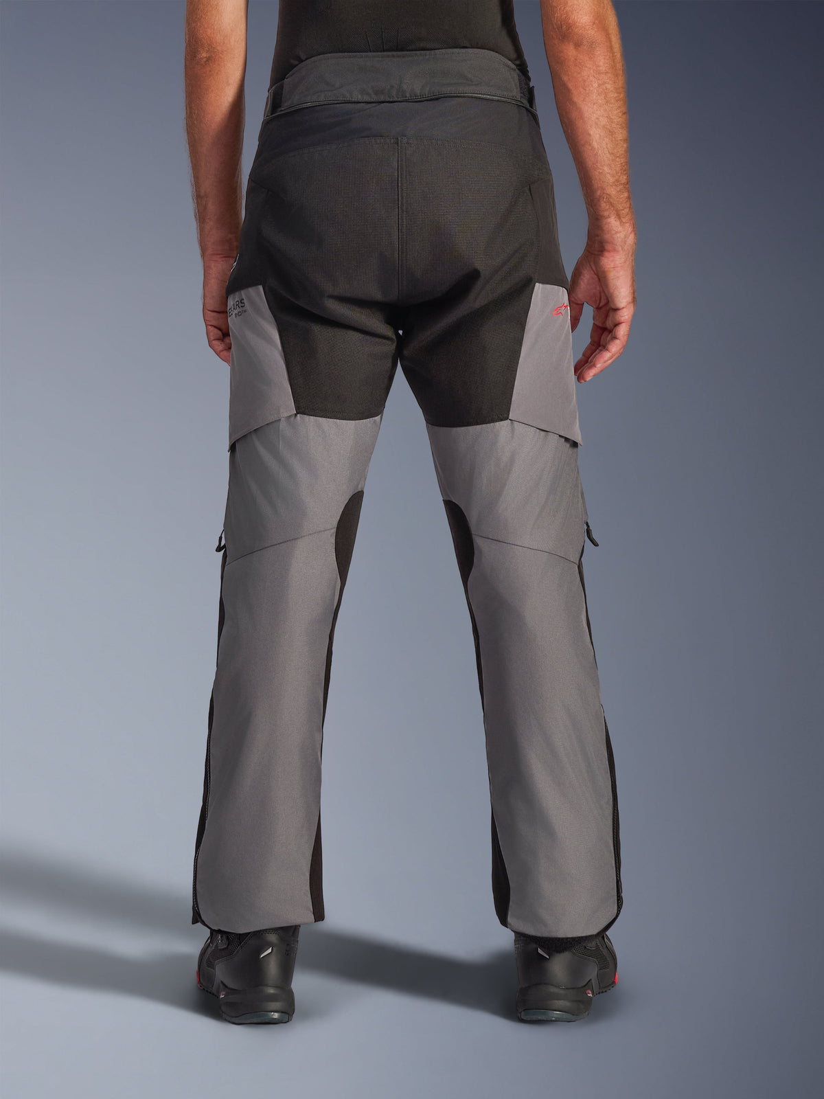 Alpinestars Andes V4 Drystar® Pants, Adventure Motorcycle Pants, Black and Dark Gray, rear view showing reinforced black seat and gray legs, featuring a small red logo, paired with black riding boots, durable textile construction for all-weather touring.