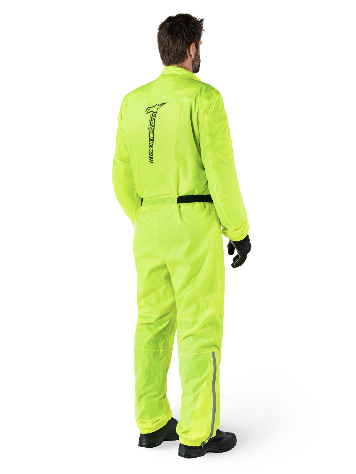 Alpinestars Hurricane Rain V2 Suit, Yellow Fluo, Rear view of a rider wearing a one-piece motorcycle rain suit, featuring a black Alpinestars logo on the back, black waist belt, and reflective strips on the lower legs, worn with black gloves and boots