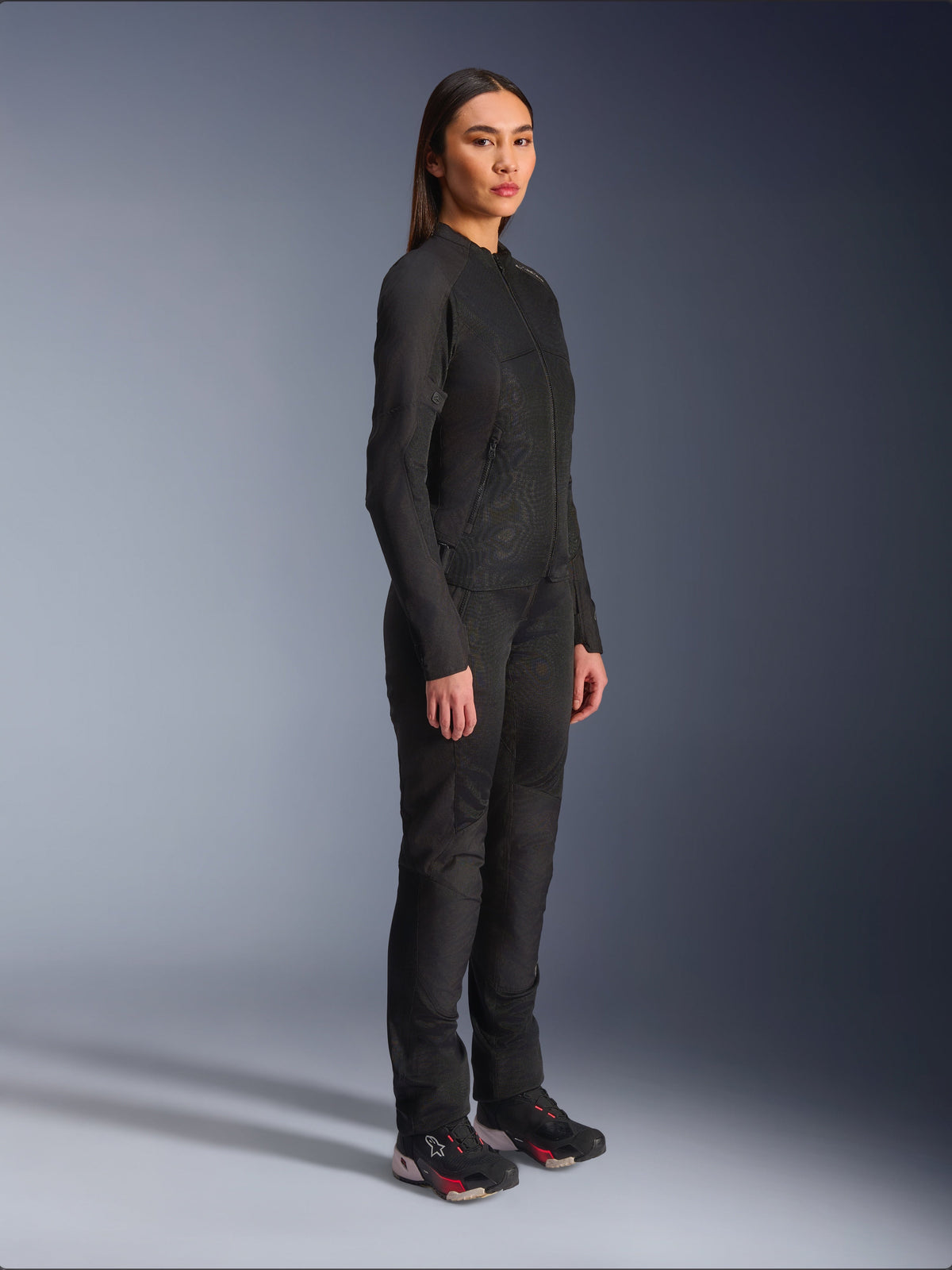 Alpinestars Woman Stella C-1 Air Jacket in Black, textile motorcycle jacket with mesh panels, worn with matching black riding pants and technical sneakers, studio shot showing a full-length urban riding outfit.