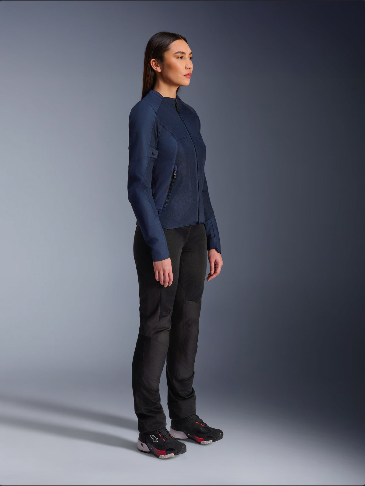 Woman wearing the Alpinestars Stella C-1 Air Jacket in Blue, urban motorcycle jacket with lightweight mesh panels for ventilation, paired with black riding pants and technical shoes, featuring a sleek profile and refined branding, studio side view