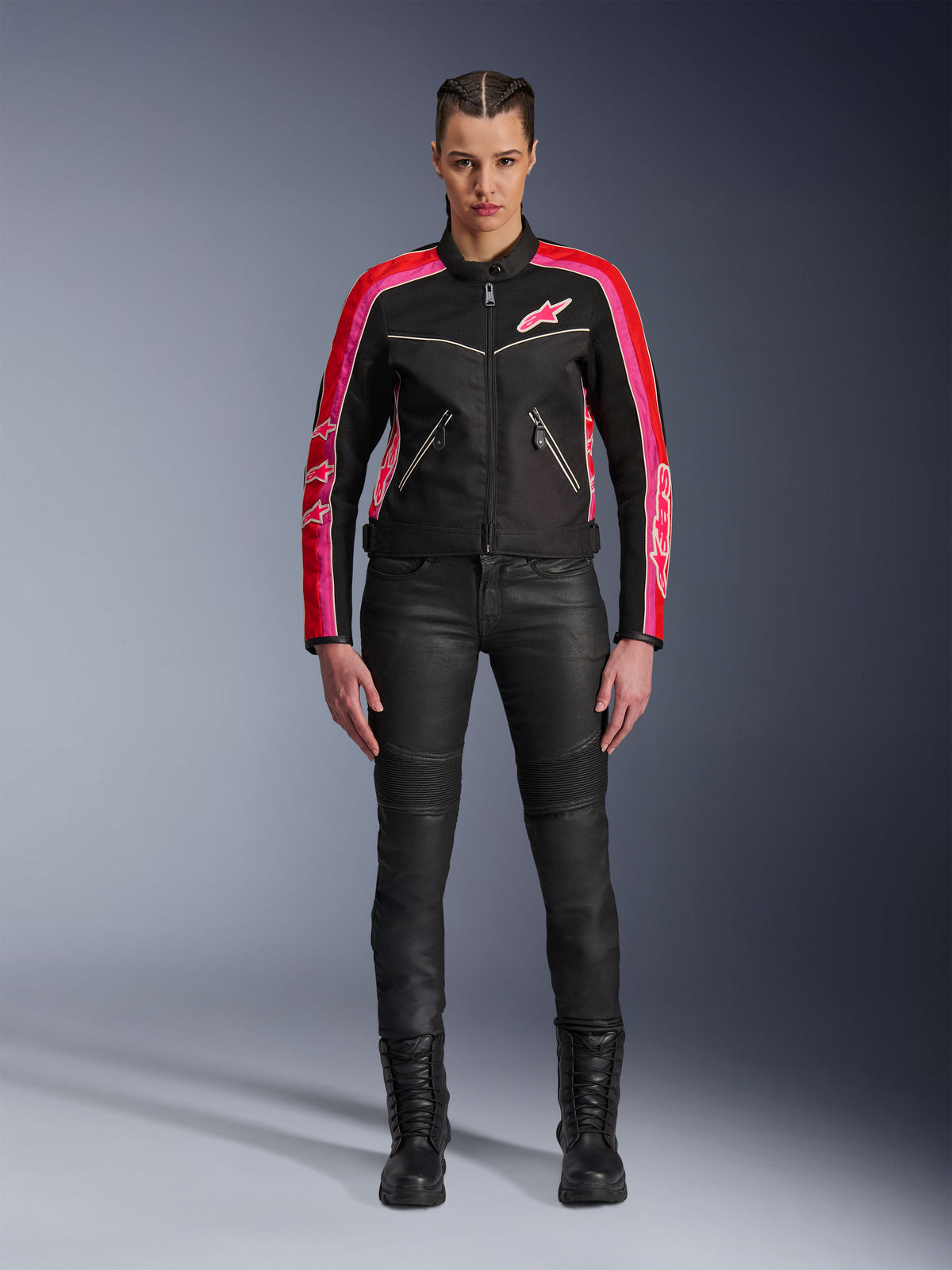 Female rider wearing the Alpinestars Stella T-Dyno Air Jacket, Black with Bright Red and Fuchsia accents, paired with black motorcycle pants and lace-up boots, featuring 3D mesh panels, tailored fit, and pink star logos, urban riding gear outfit