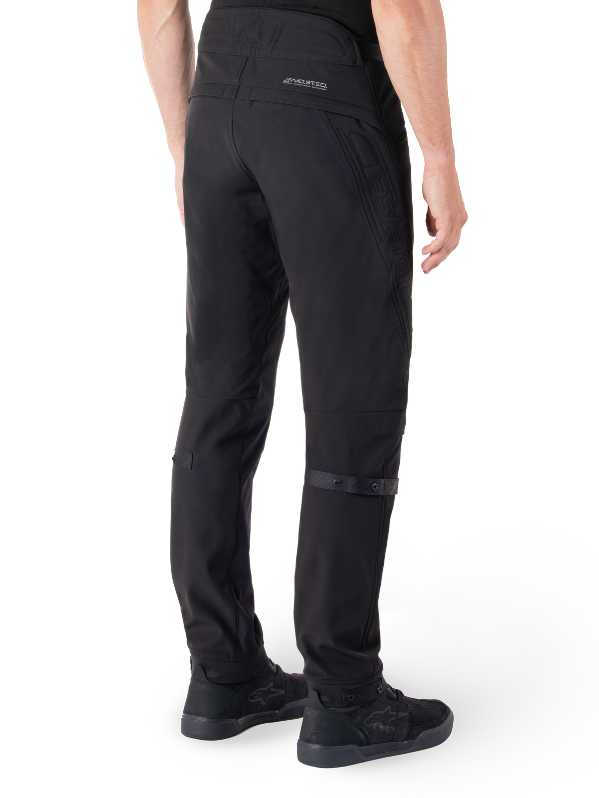 Alpinestars Alden Pants, Urban Motorcycle Pants, Black, rear view showing technical softshell fabric with quilted details, MO.ST.EQ. reflective branding on the back yoke, and adjustable calf straps, paired with black riding shoes
