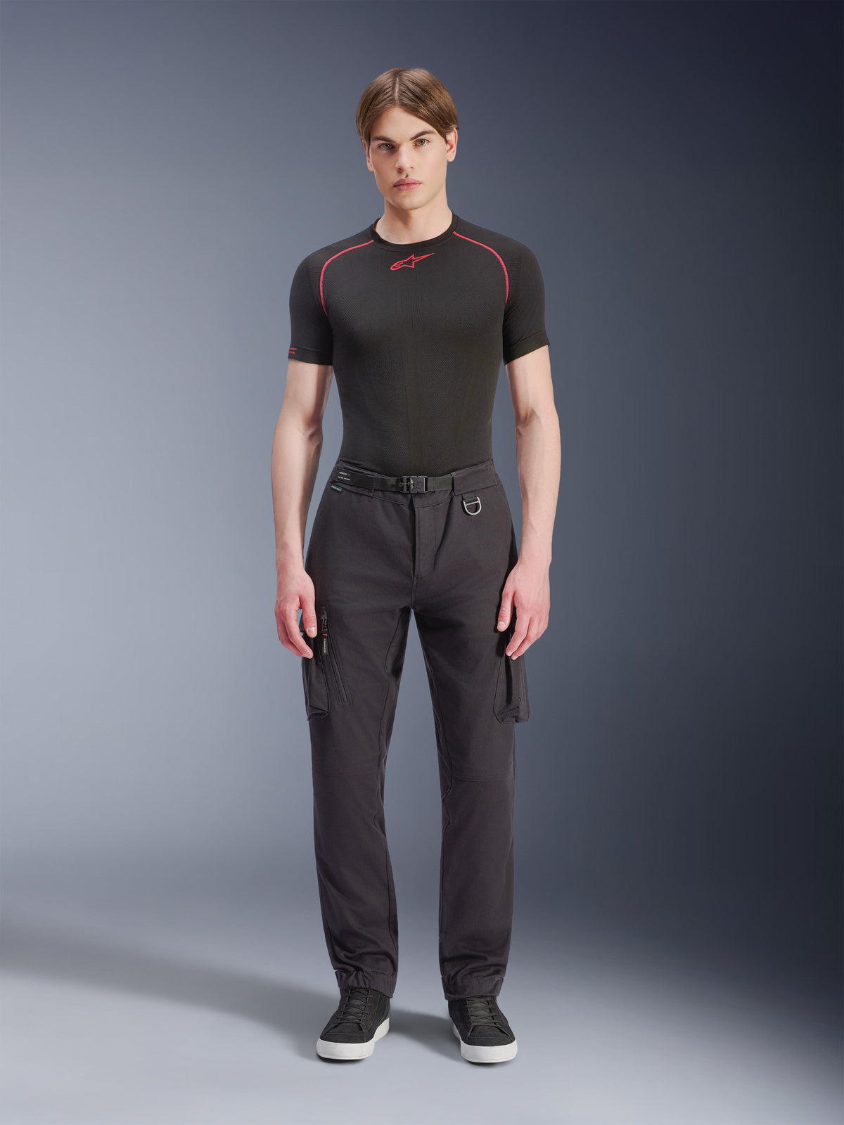 Alpinestars Flex-AST Cargo Pants - Short, Black, worn by a male model with a black performance t-shirt and black sneakers, urban motorcycle pants featuring multiple cargo pockets, a tapered fit, and a built-in belt with buckle and D-ring