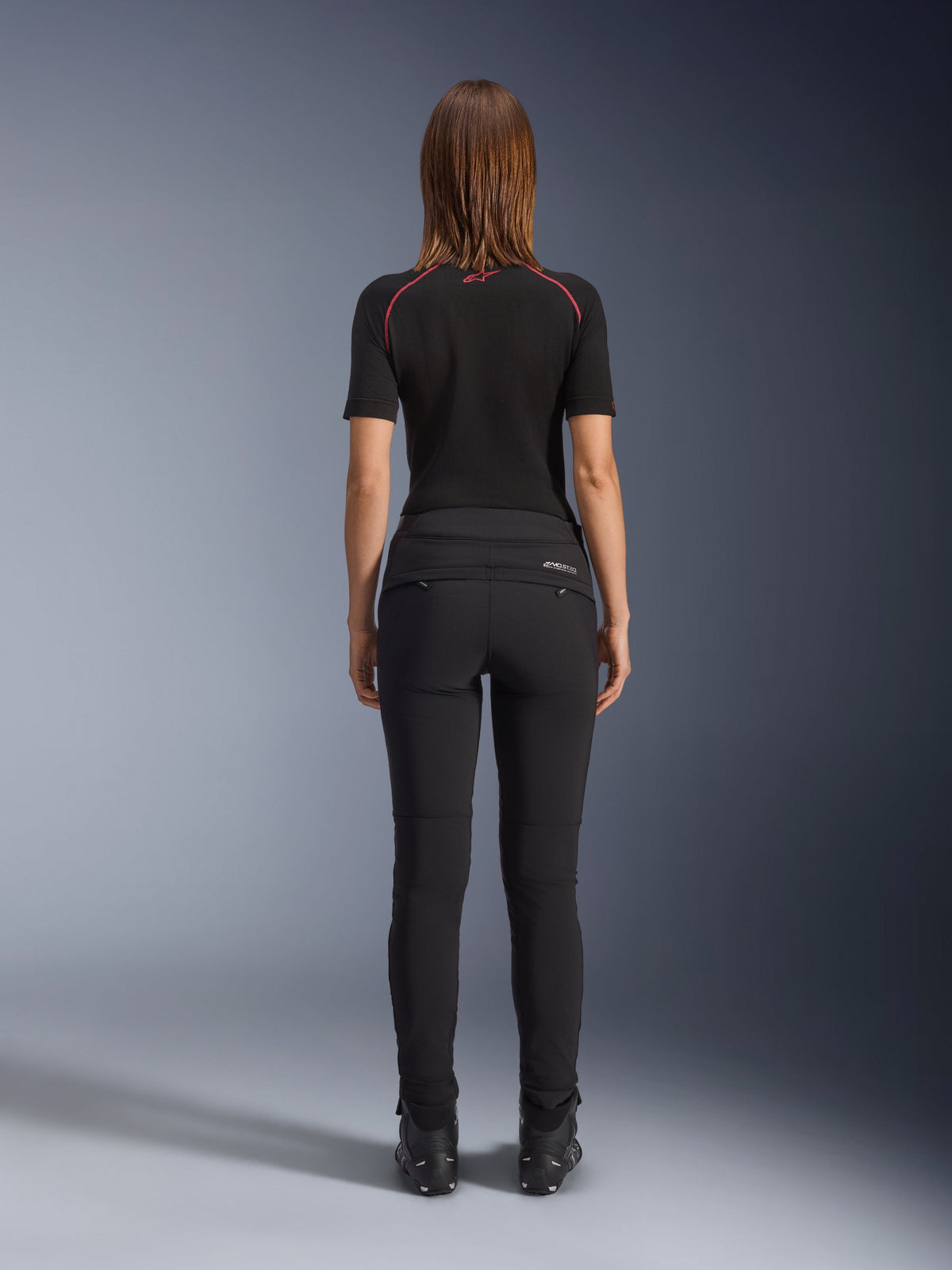Alpinestars Alamosa Women Pants, Black, rear view showcasing slim-fit textile construction, zippered back pockets, and reflective MO.ST.EQ. branding on the back yoke, worn with a black short-sleeve base layer and black motorcycle boots